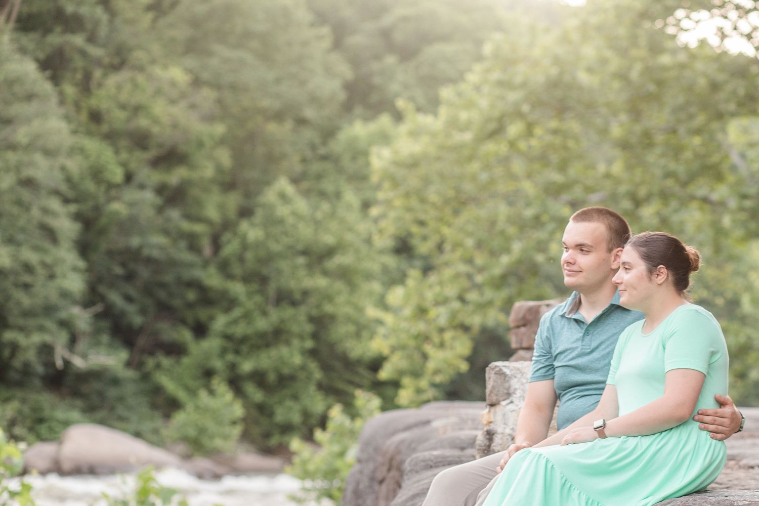 A couple shares tender moments together on rocks near a waterfall in matching mint and gray outfits.