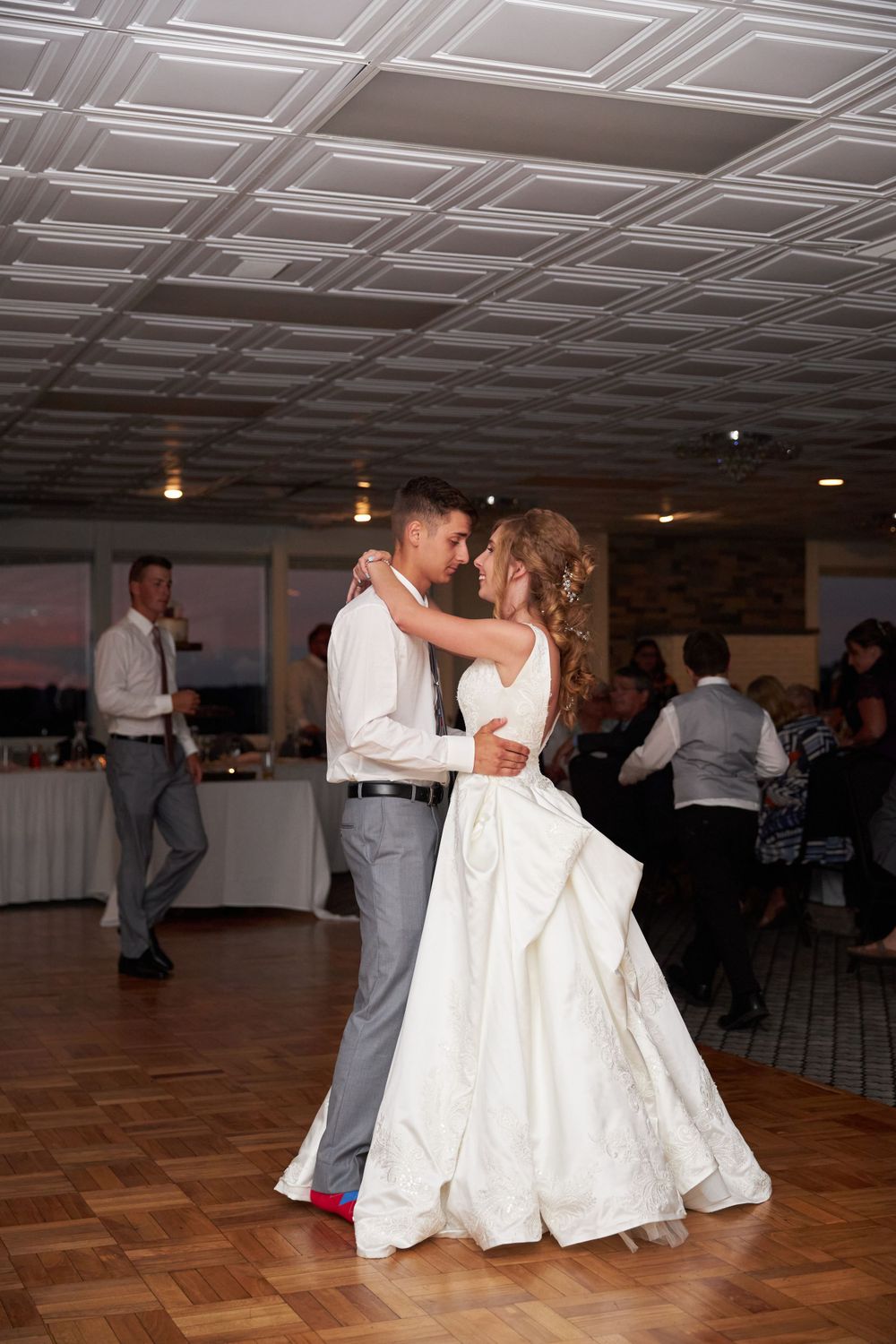 Newlyweds sharing their first dance in a reception hall with decorative ceiling.