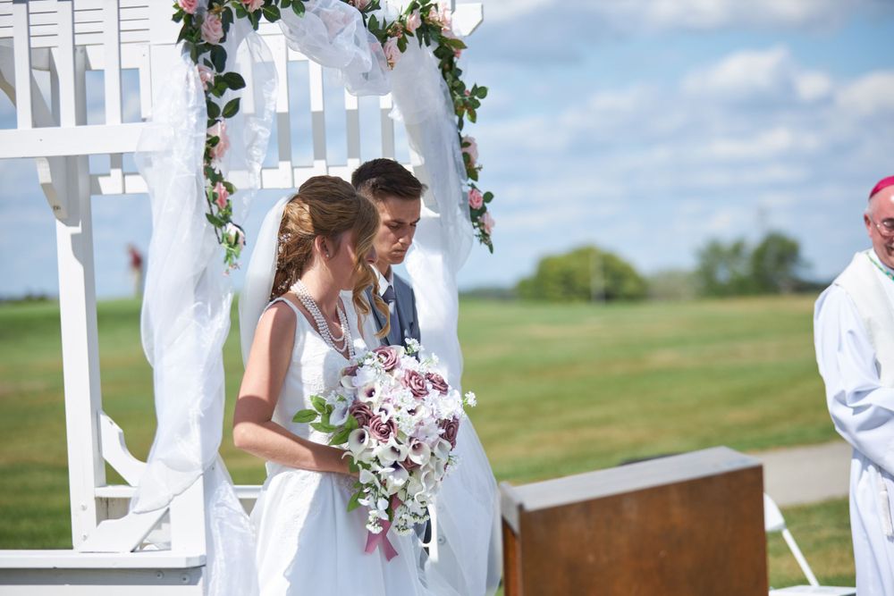 Couple standing under a floral arch during an outdoor wedding ceremony.