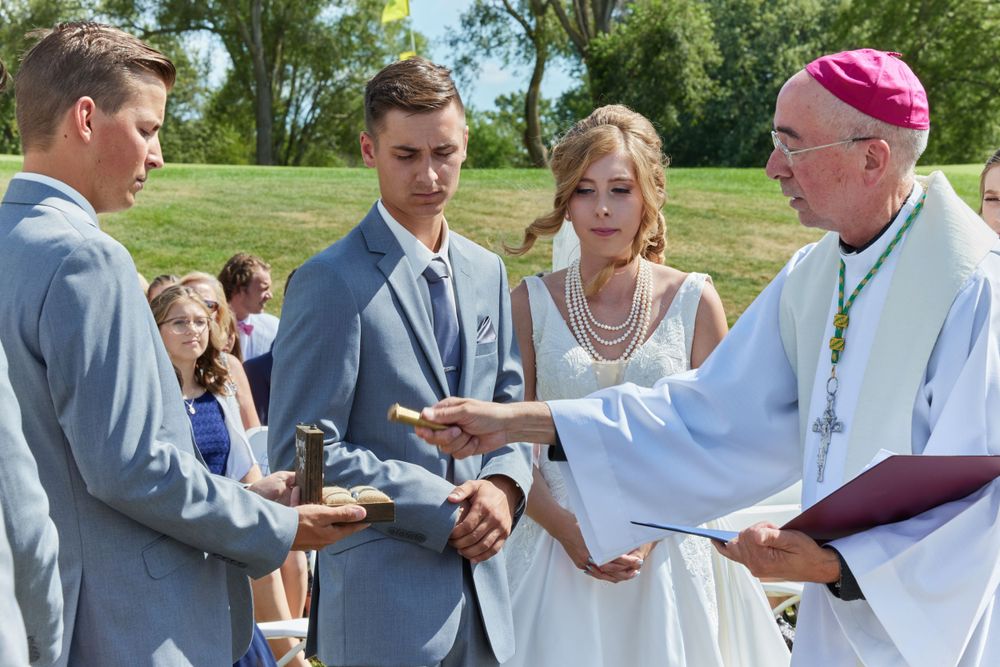 Religious officiant conducting outdoor wedding ceremony with couple and attendant.