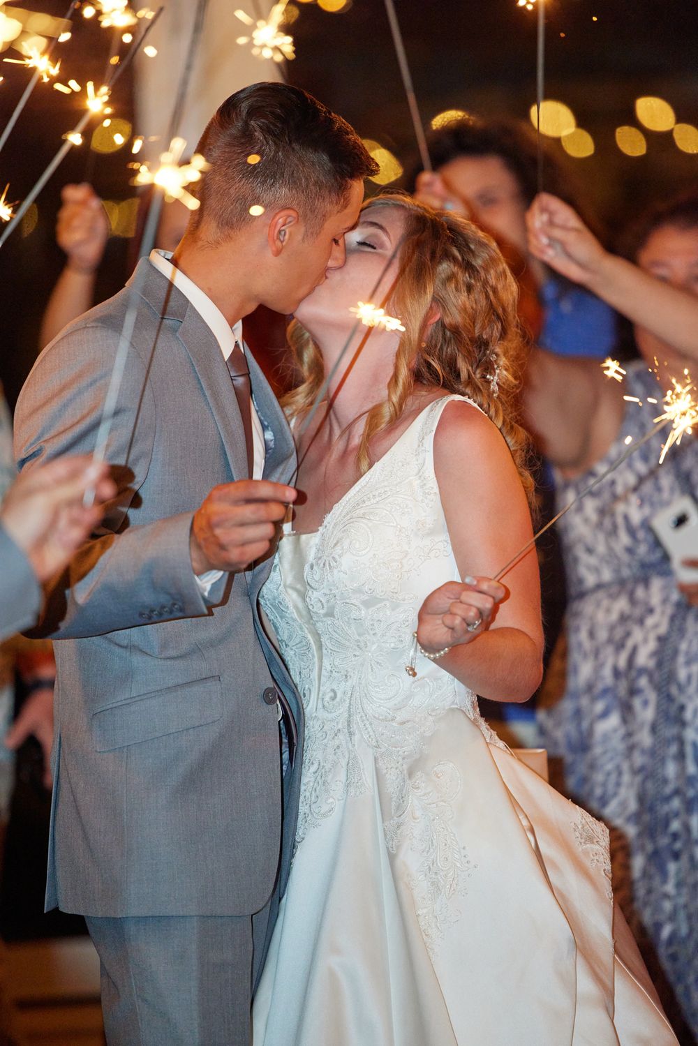Couple sharing romantic kiss during sparkler exit at wedding reception.
