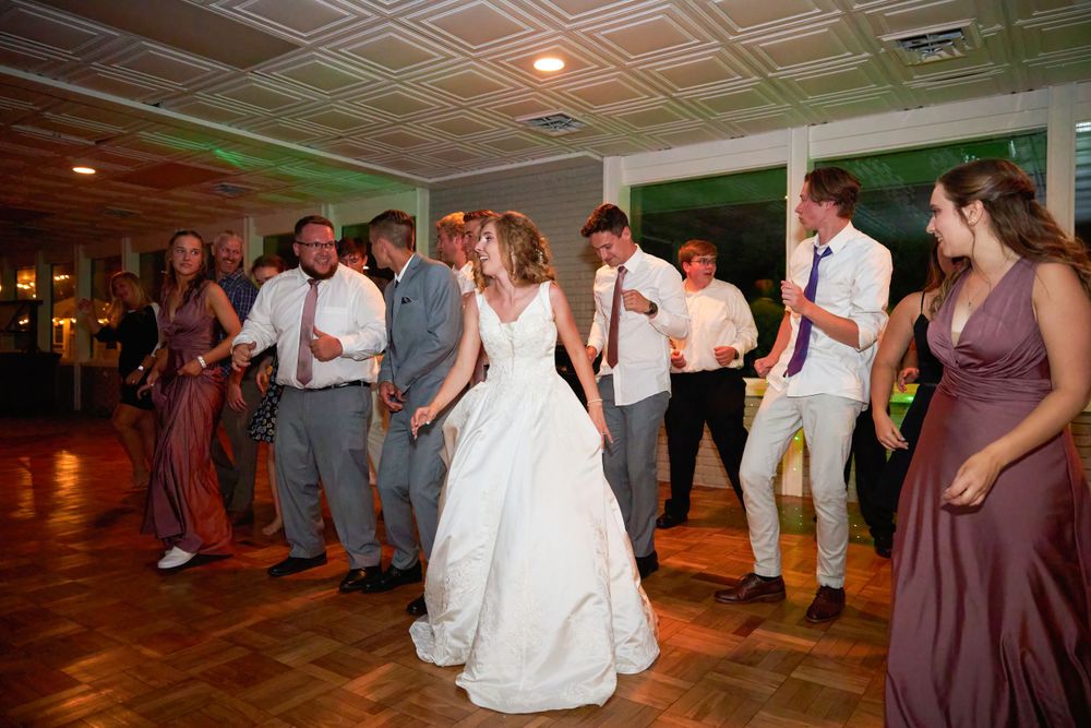 Wedding party dancing together on wooden dance floor at indoor reception.