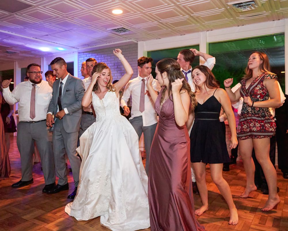 Wedding guests dancing and celebrating at lively reception with purple lighting.