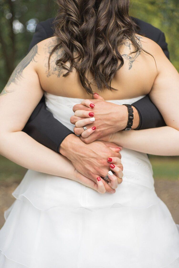Close-up of embracing couple's hands with red nail polish against a white wedding dress.
