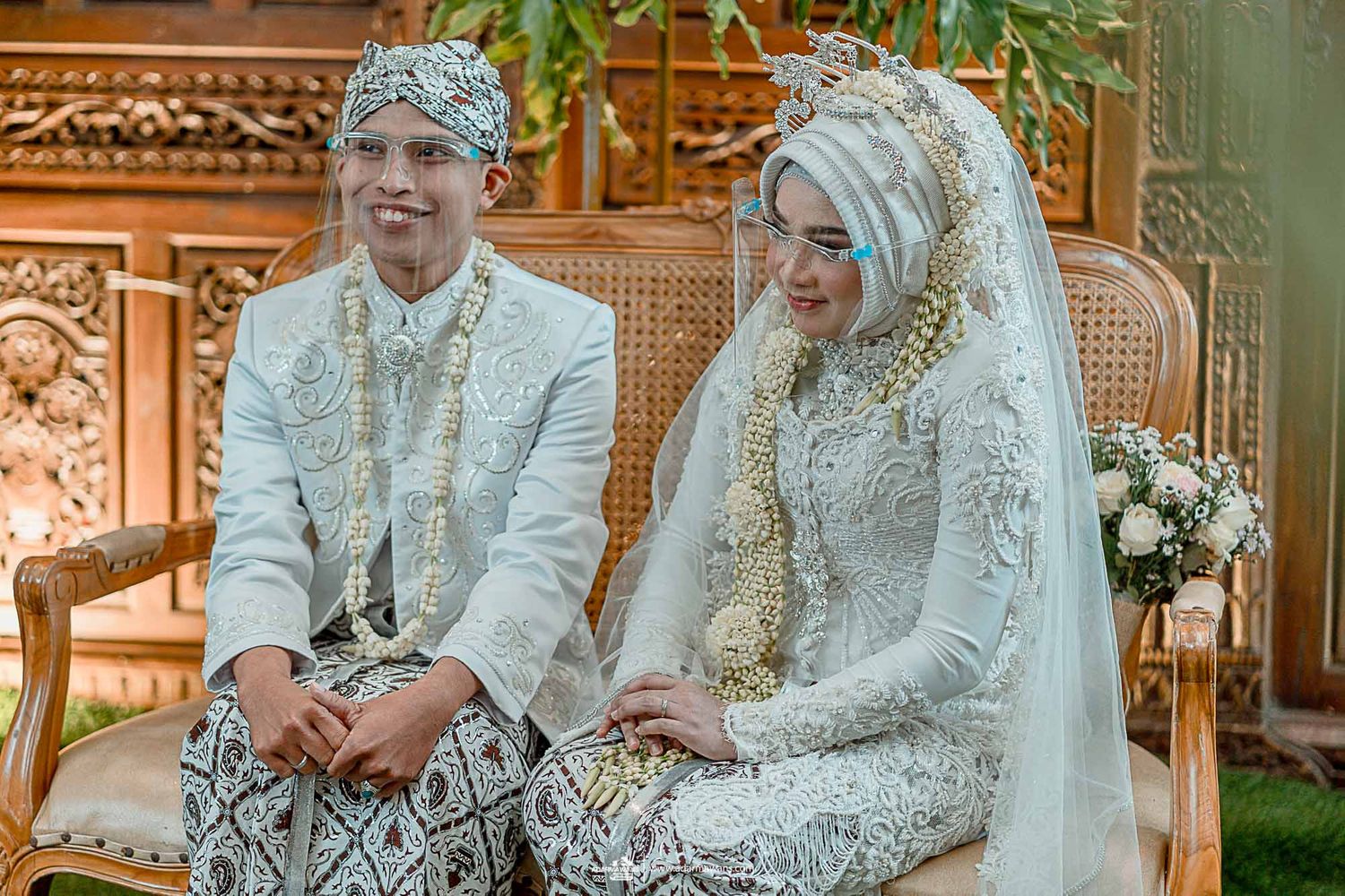 Traditional Javanese wedding couple seated in ornate ceremonial chairs during their wedding ceremony.