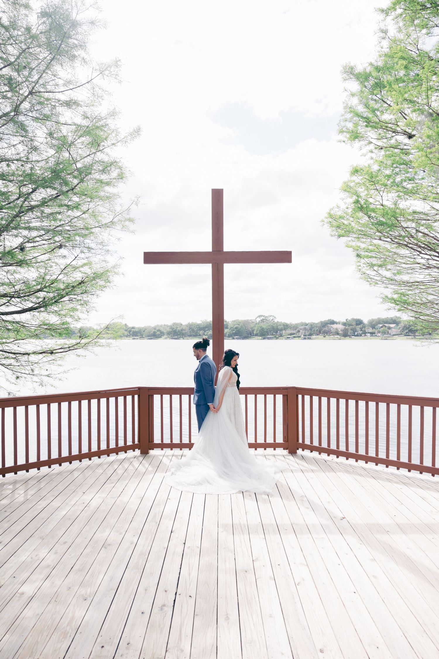 Wedding ceremony setting on a wooden deck with a cross and trees in the background.