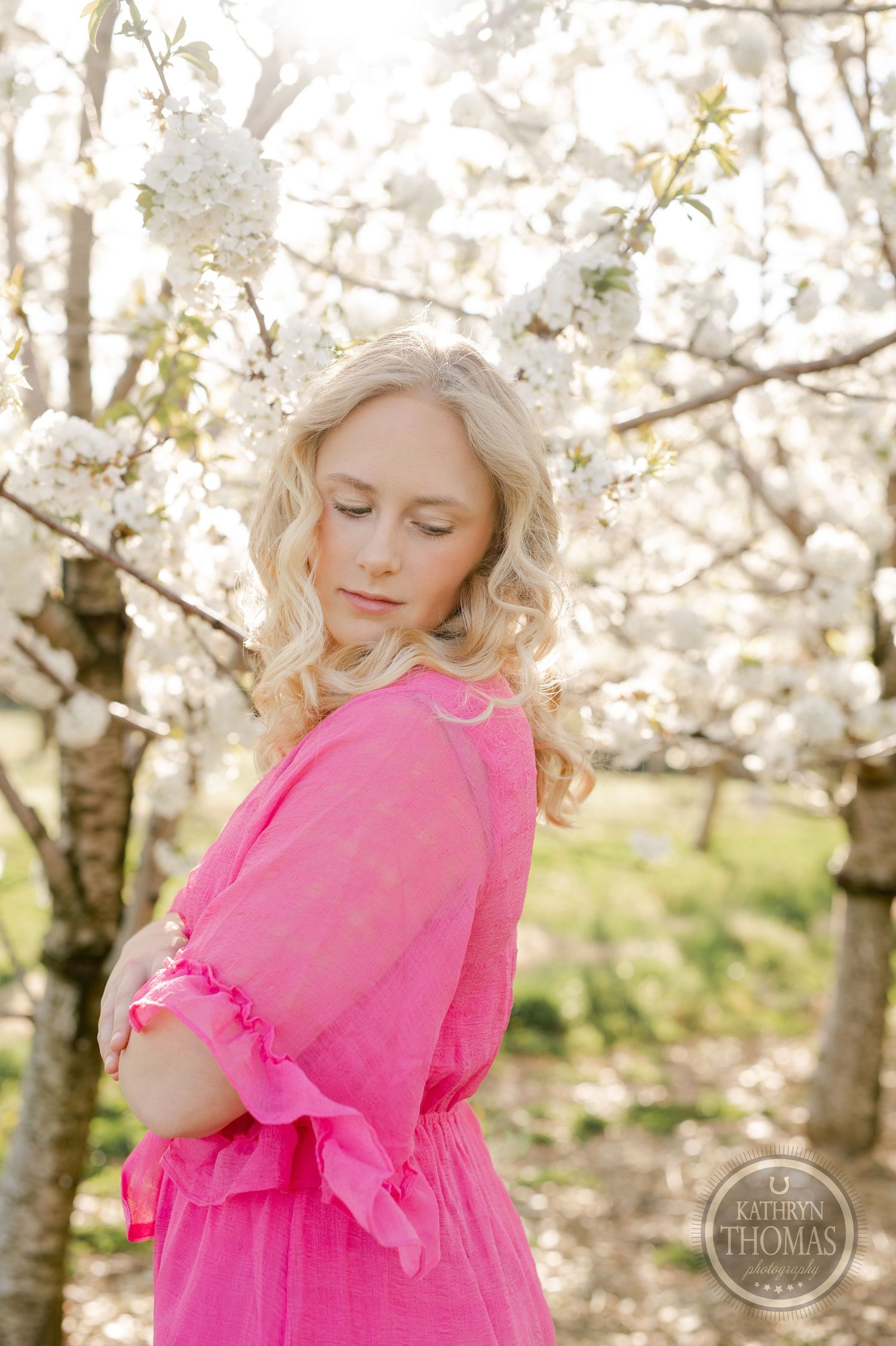 Dreamy spring portrait in a pink dress surrounded by cherry blossom trees.