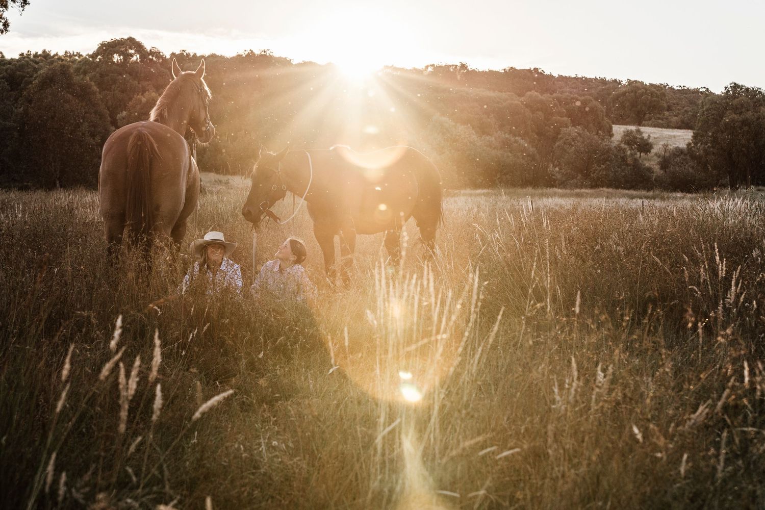 two teenage rural kids sitting in the long grass paddock with the sun setting behind the hills.