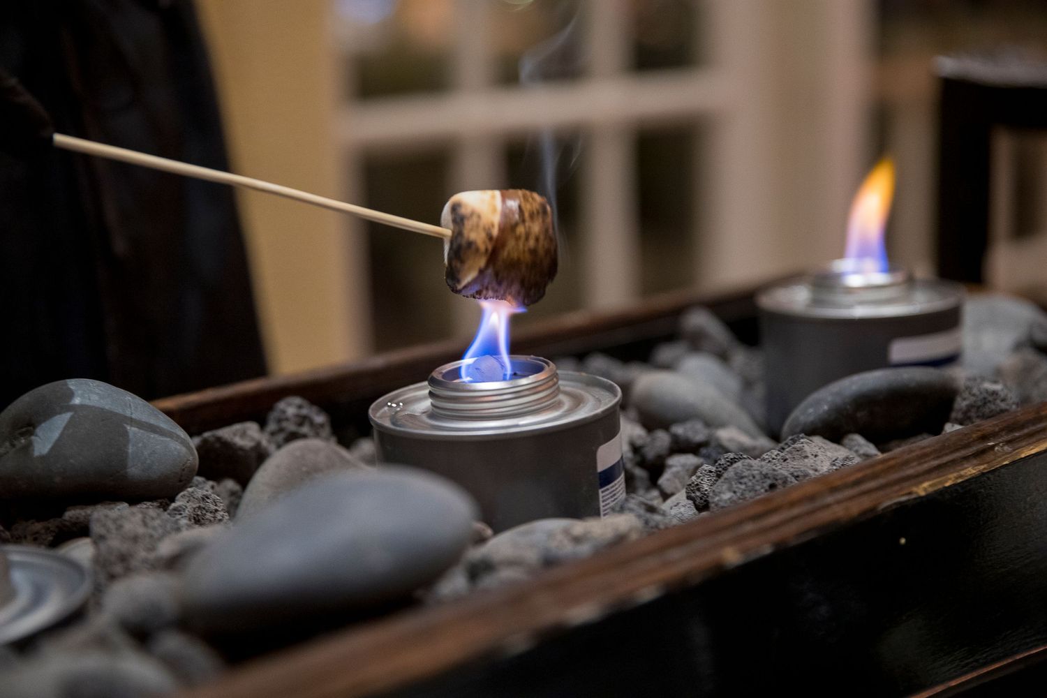 Marshmallow being roasted over small blue flame at dessert station.