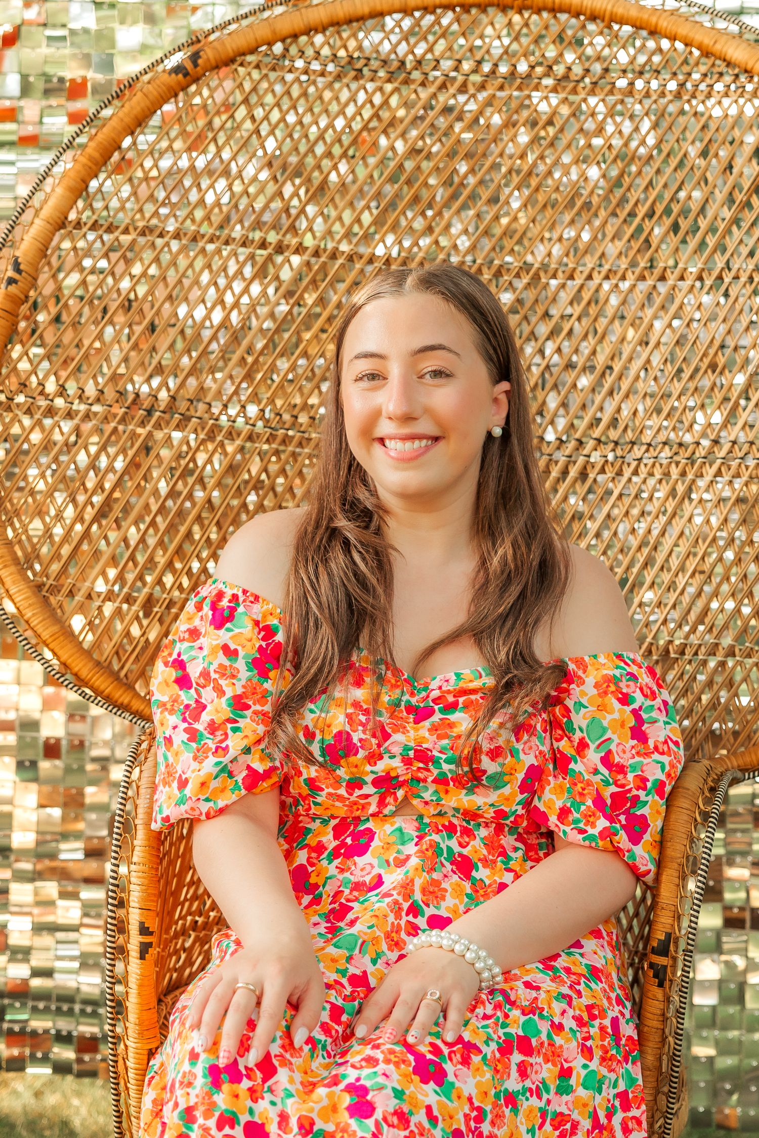 Colorful floral dress stands out against a woven peacock chair and metallic backdrop.