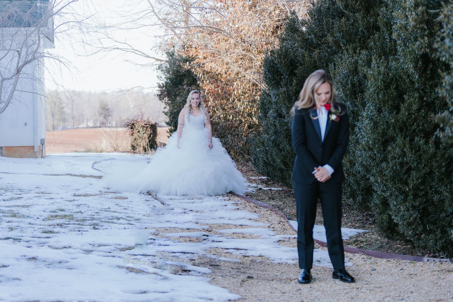 Winter wedding first look scene with evergreen backdrop and snowy ground.