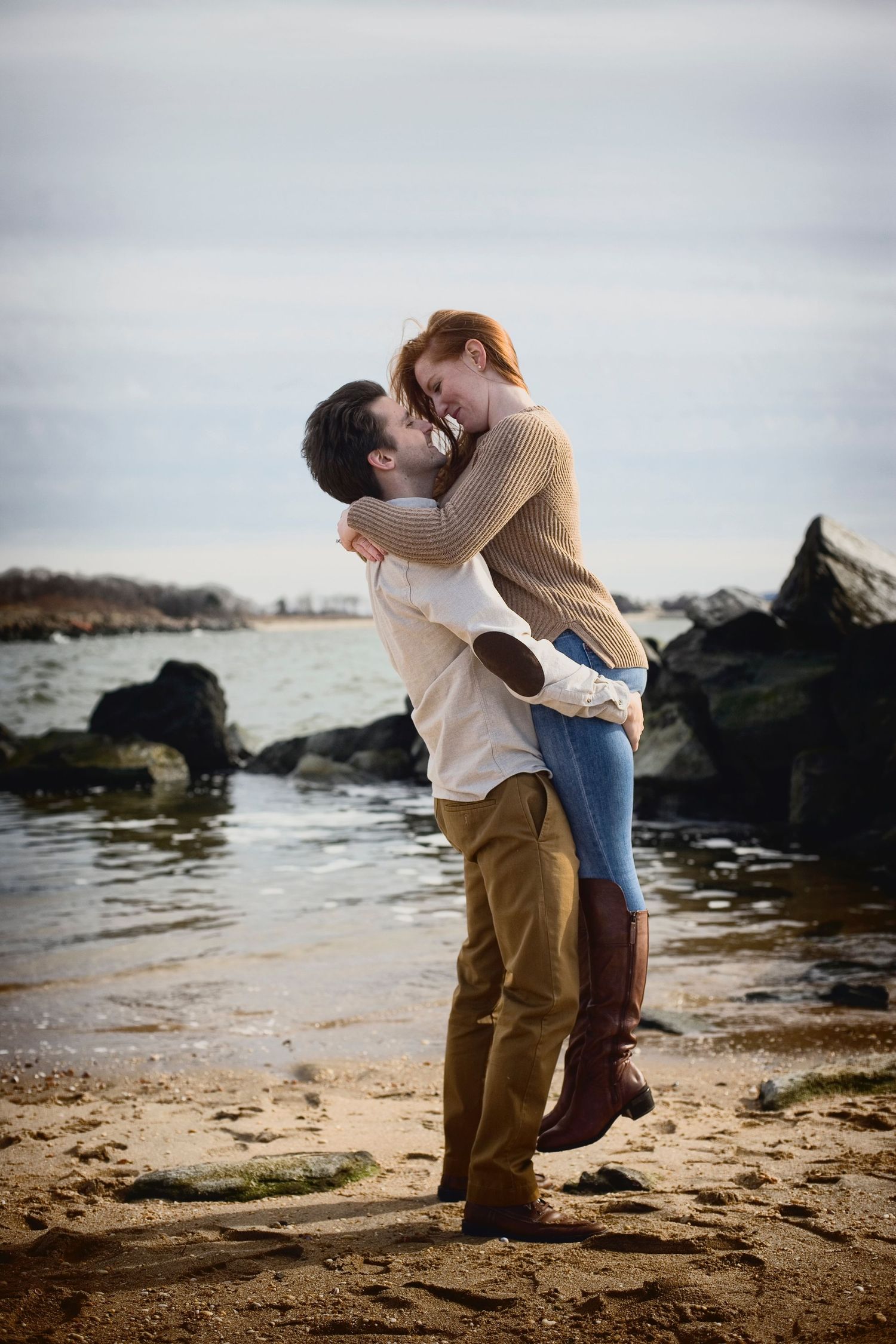 couple embracing while standing on rocks near a body of water, in the style of alex hirsch