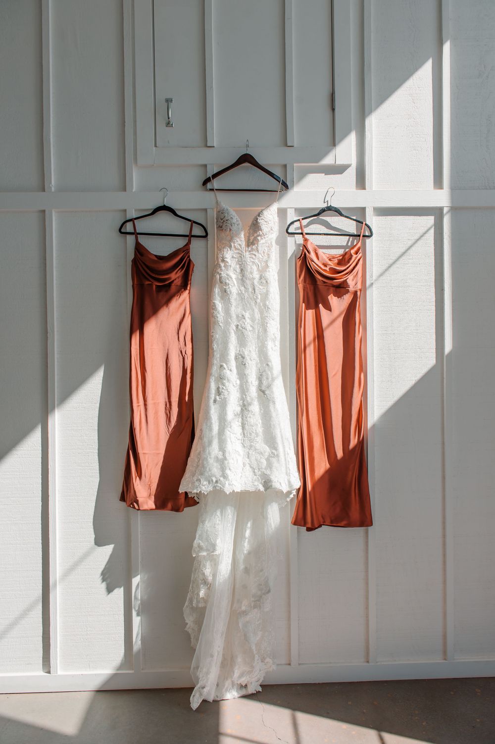 White and coral colored dresses hanging on a white paneled wall in natural light.