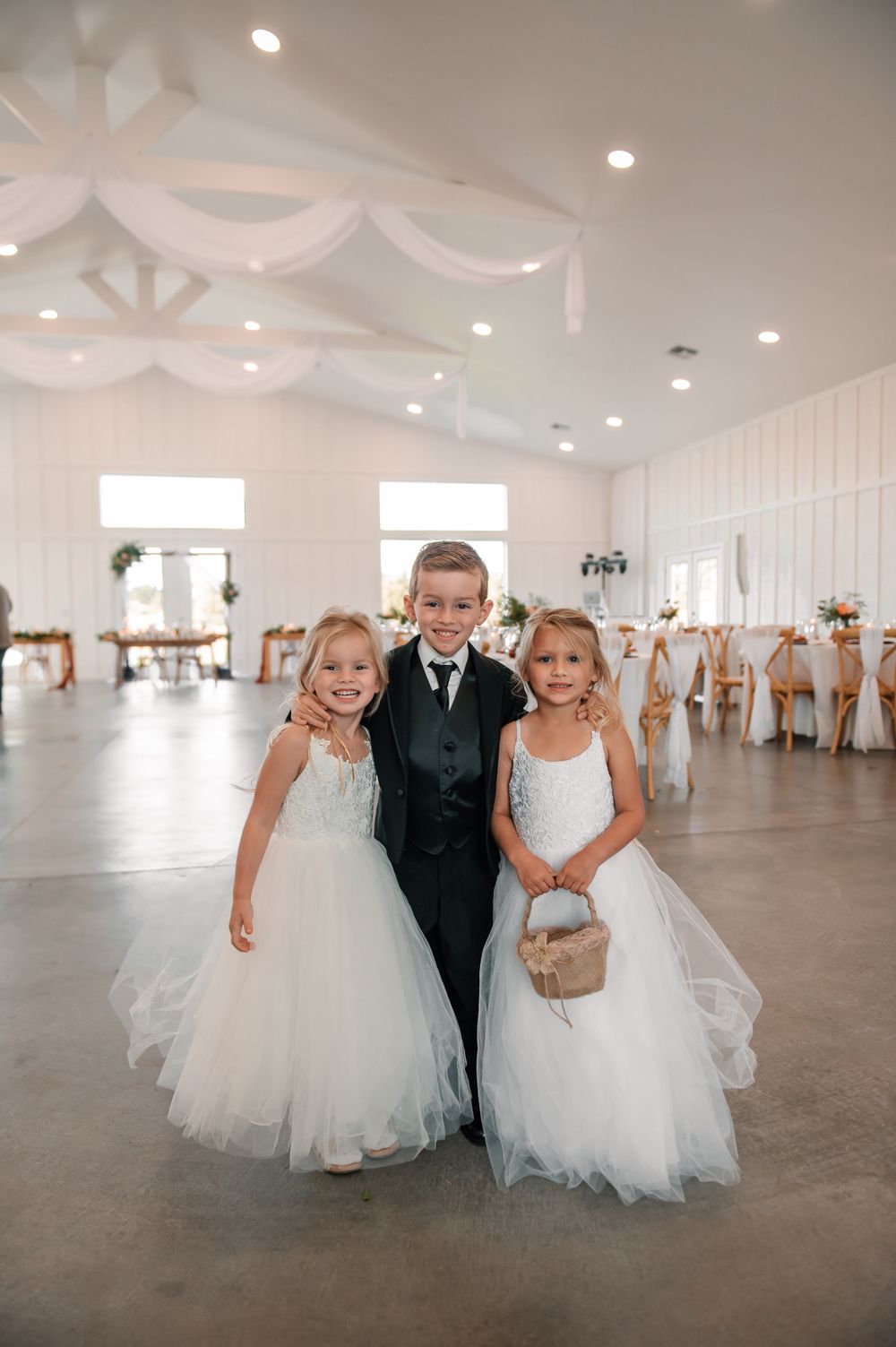 Young attendants in formal white dresses walking through an elegant white reception venue.