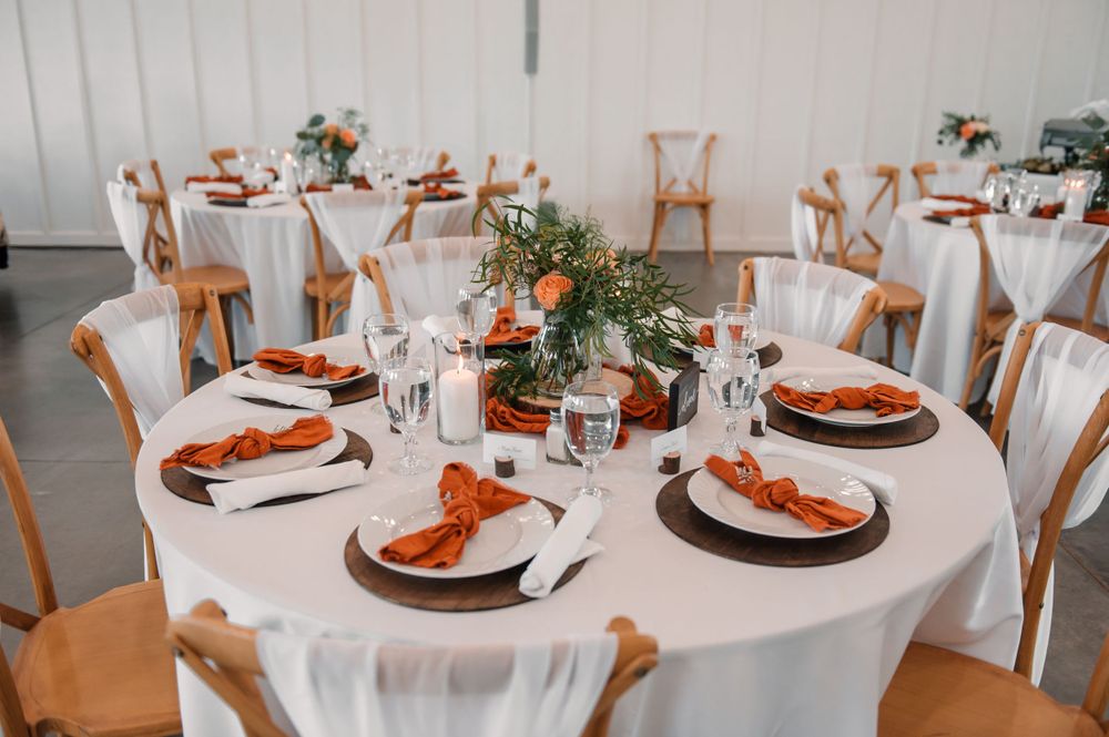 Wedding reception tables set with white linens and copper accents in an elegant indoor venue.
