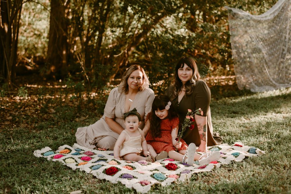A casual outdoor gathering on a colorful quilt blanket in dappled sunlight.
