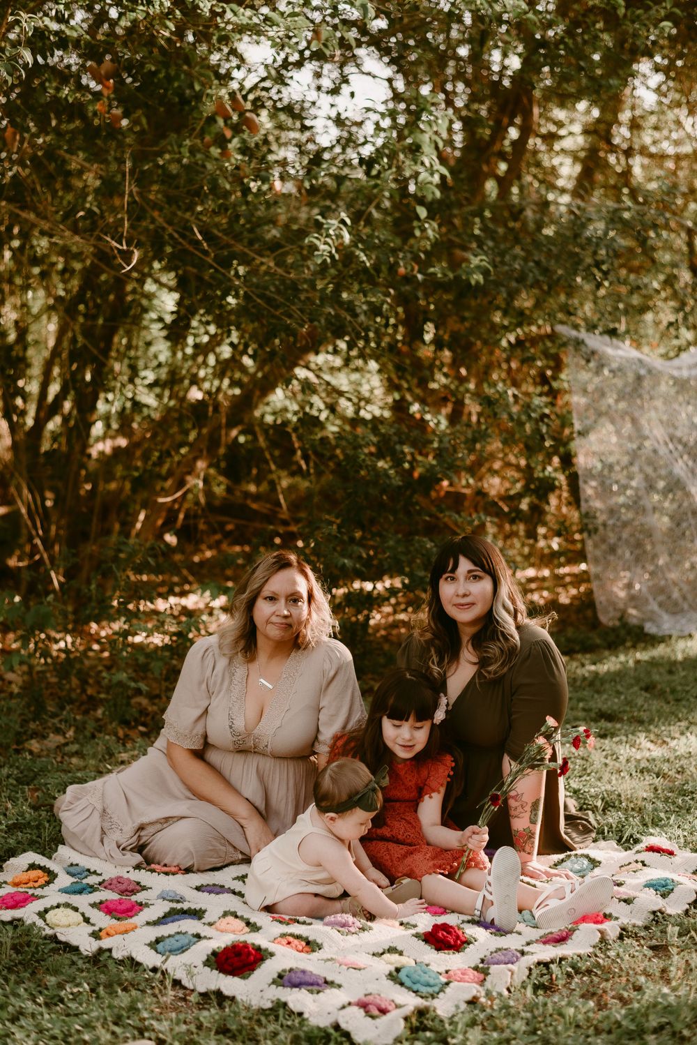 A picnic scene with a floral blanket spread out in a sunlit wooded area.