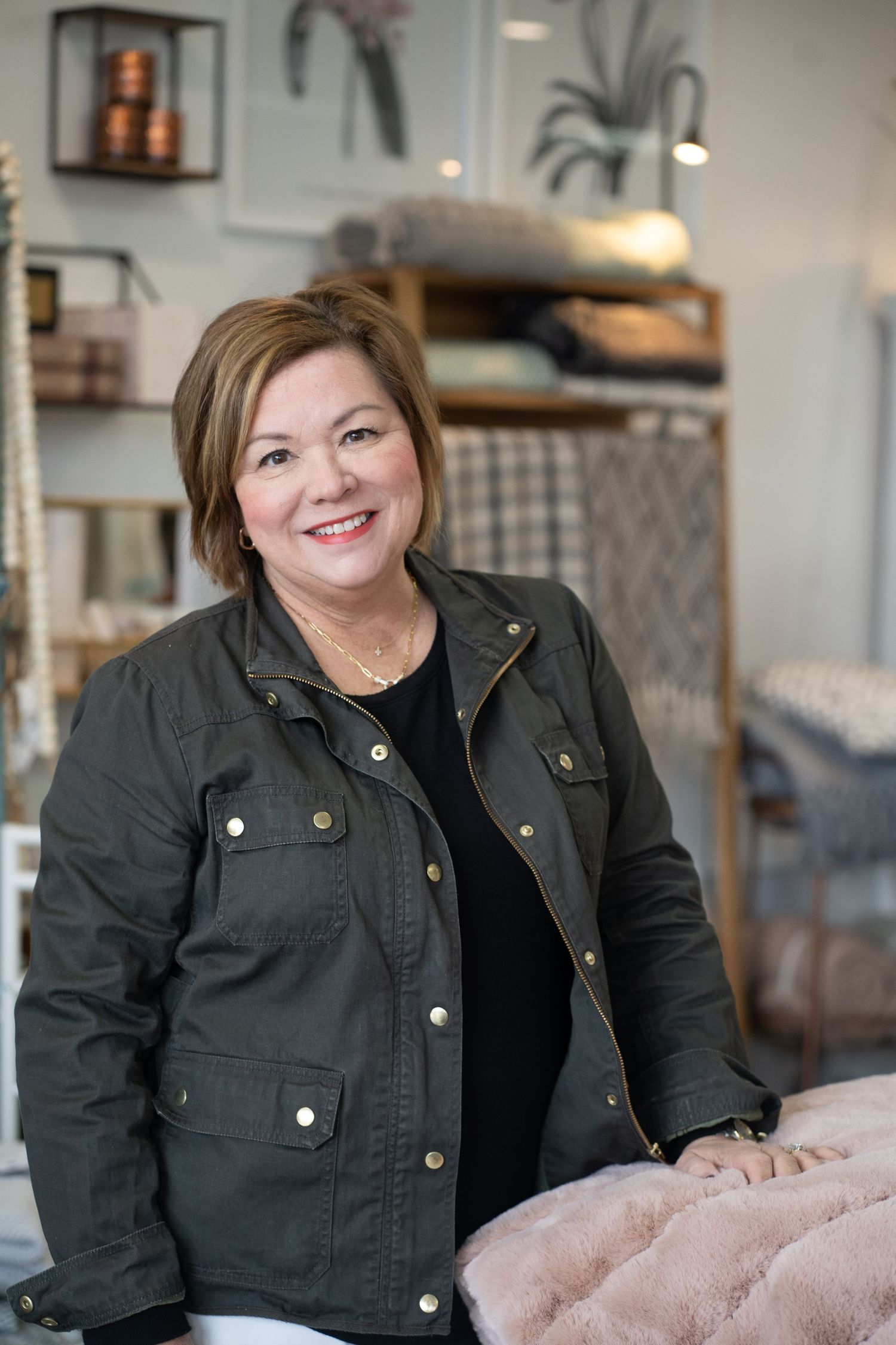 Retail worker in olive utility jacket smiles inside home goods store with decor in background.