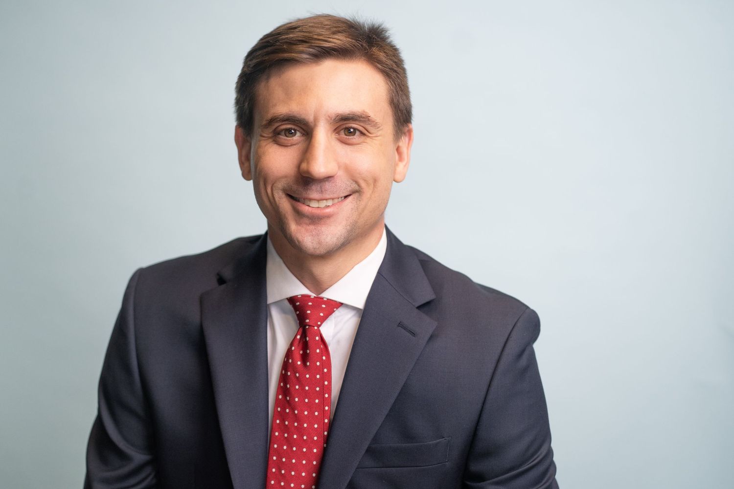 Professional business headshot of man in dark suit and red polka dot tie.