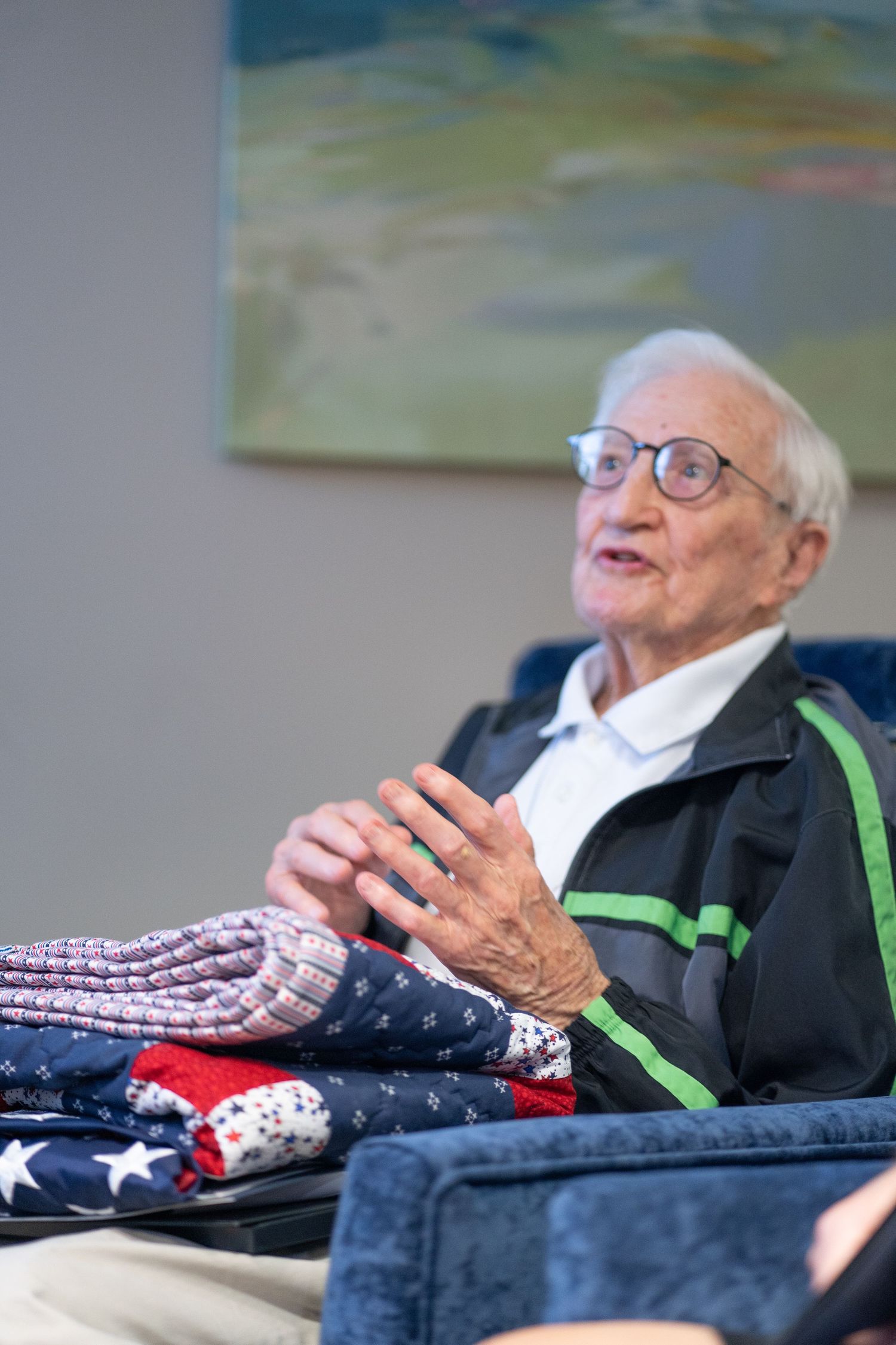 Elderly man in glasses sitting with folded American flags.