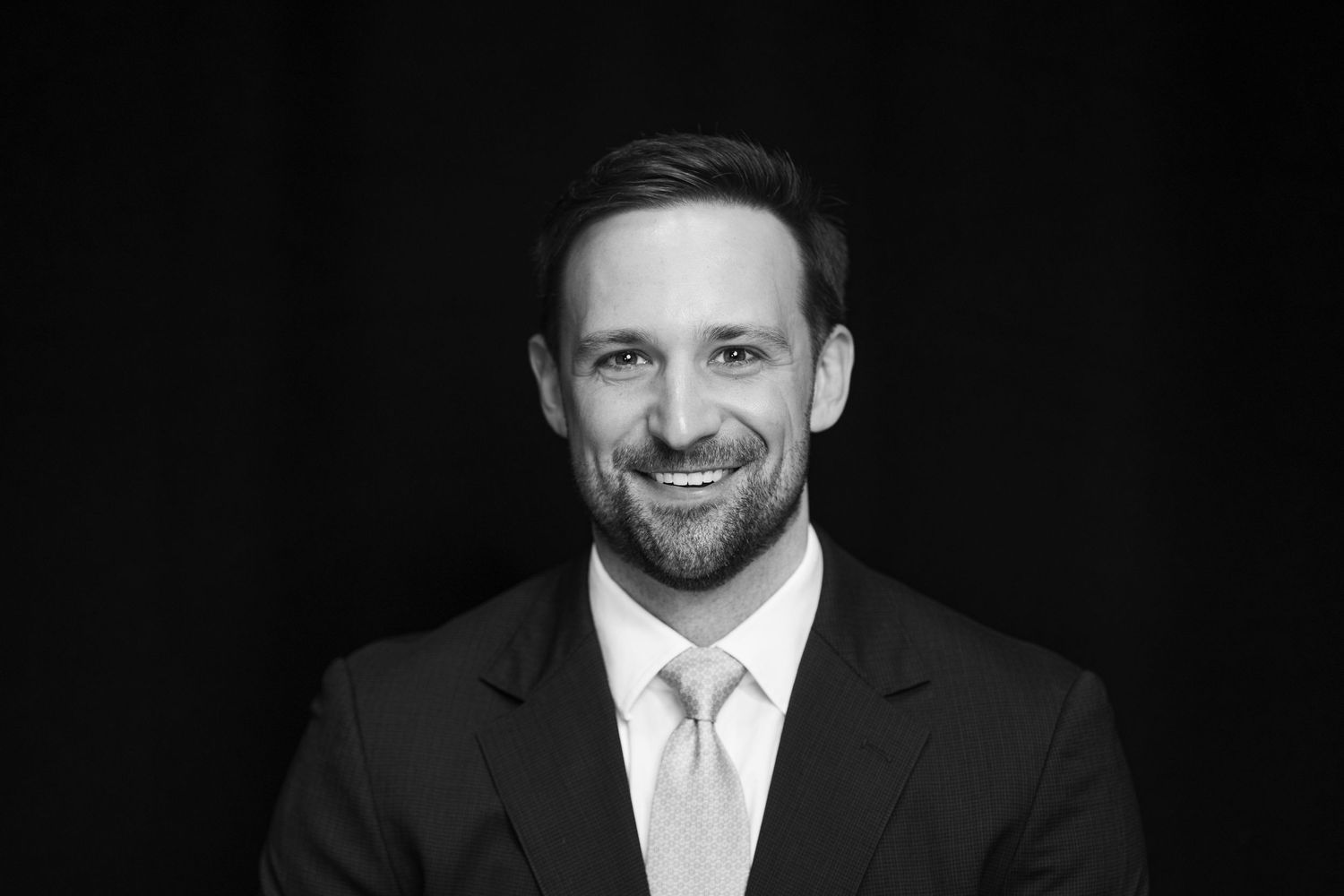 Professional black and white portrait of businessman against dark background.