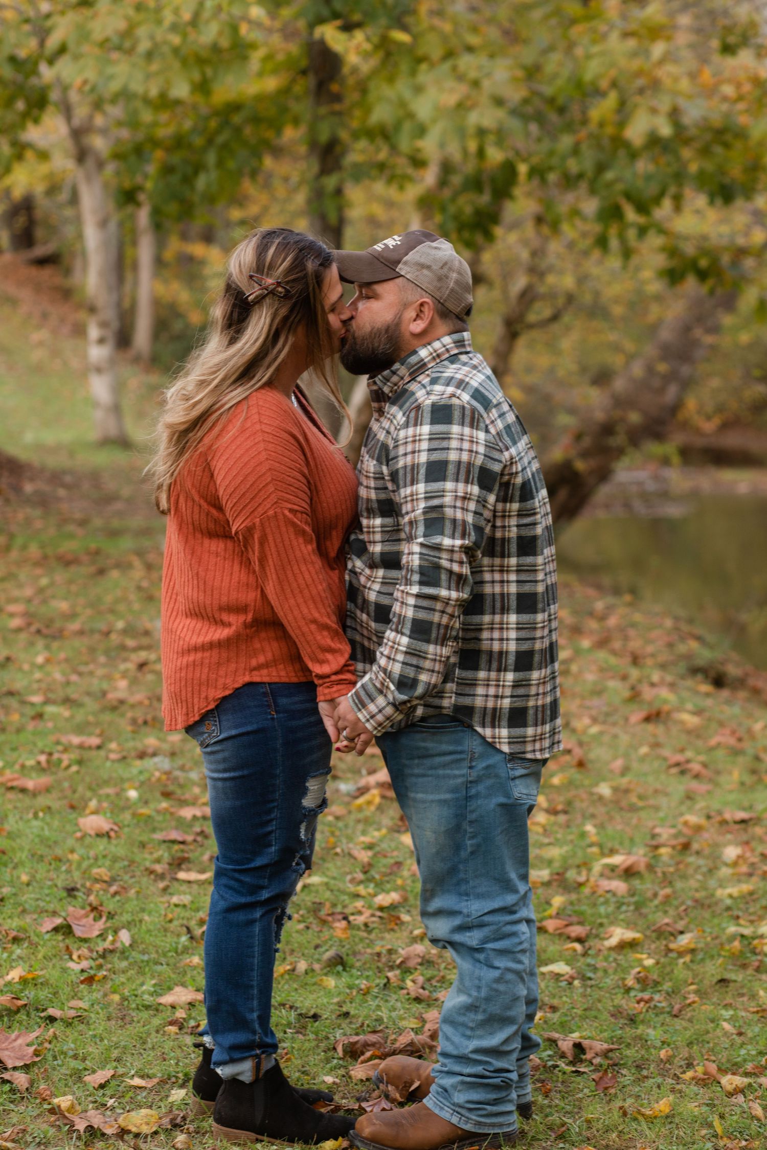 A couple shares intimate moments on fallen autumn leaves by a pond.