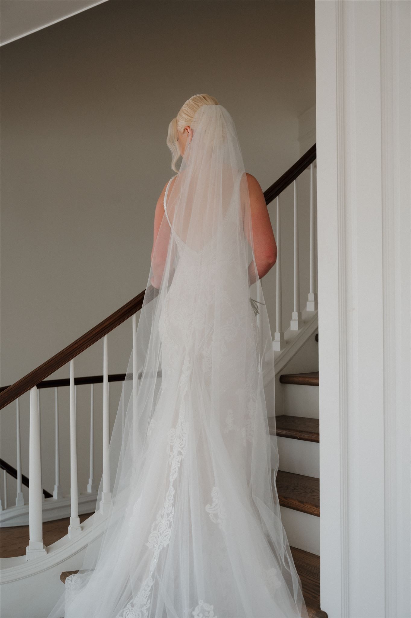 Back view of wedding dress and cathedral veil as bride ascends elegant staircase.