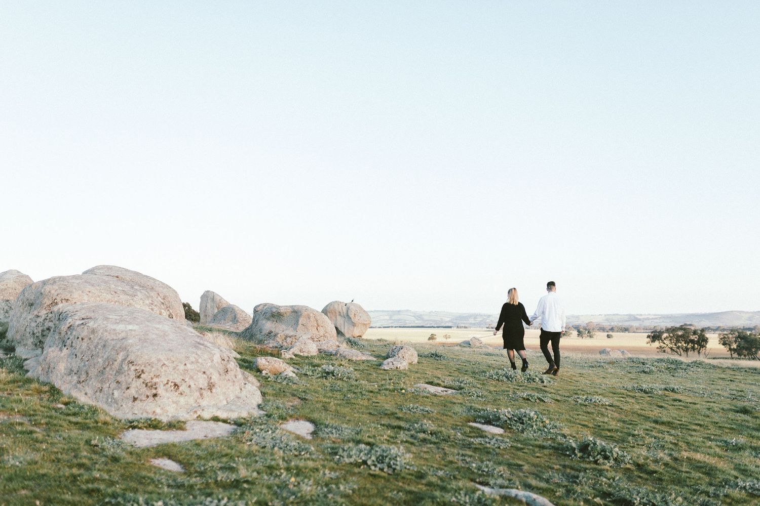 Two figures and a dog walking among large boulders in a natural landscape.