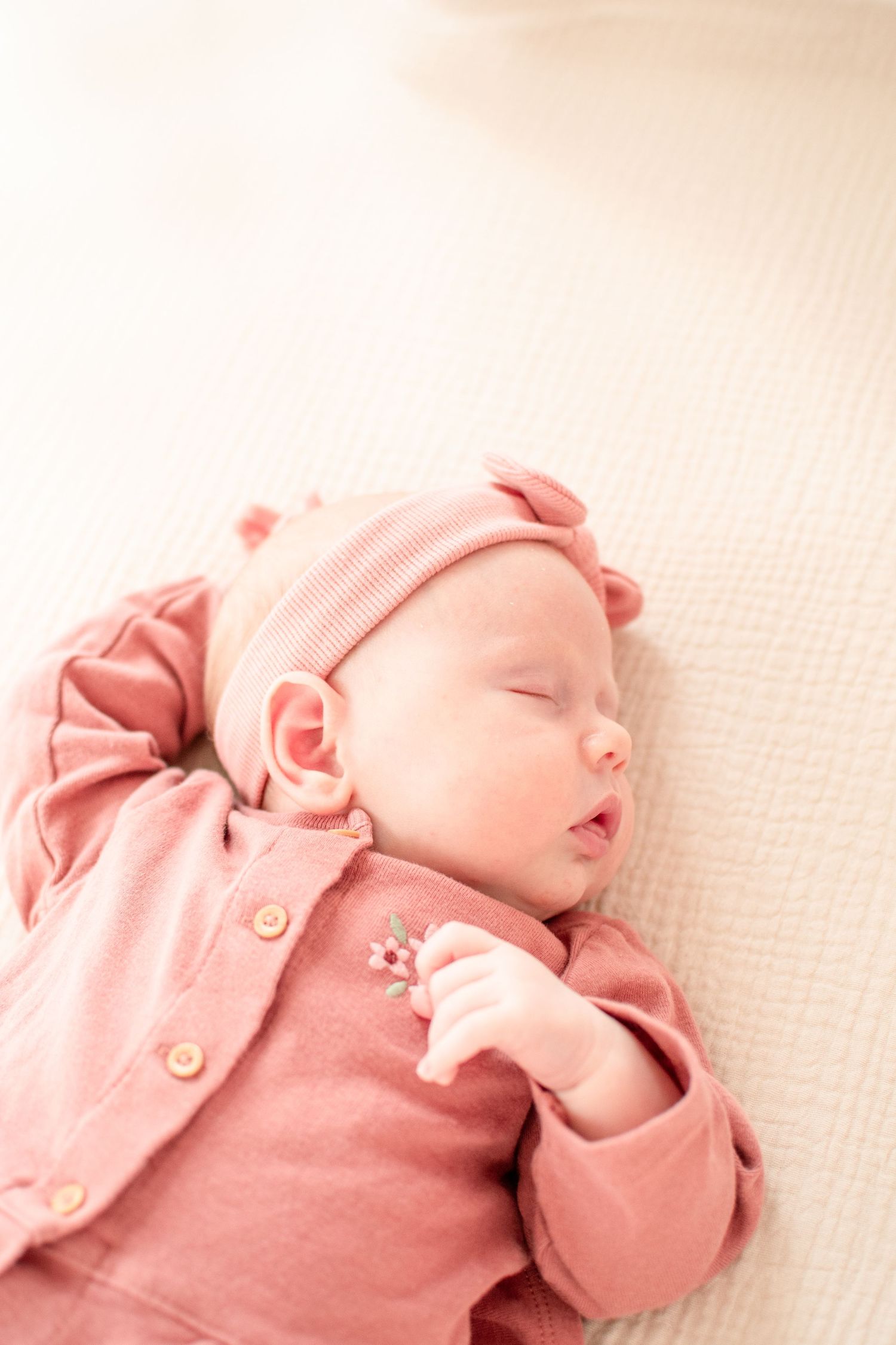 Sleeping newborn in pink outfit against textured cream background.