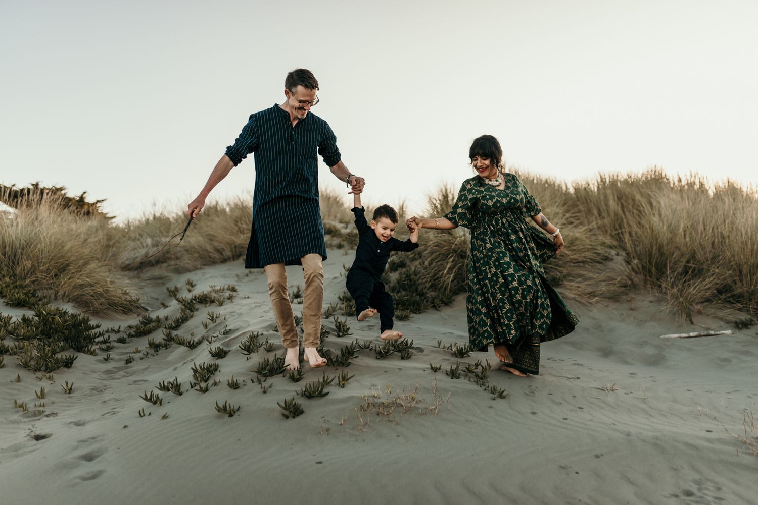 Family holding hands while jumping together on sandy beach.