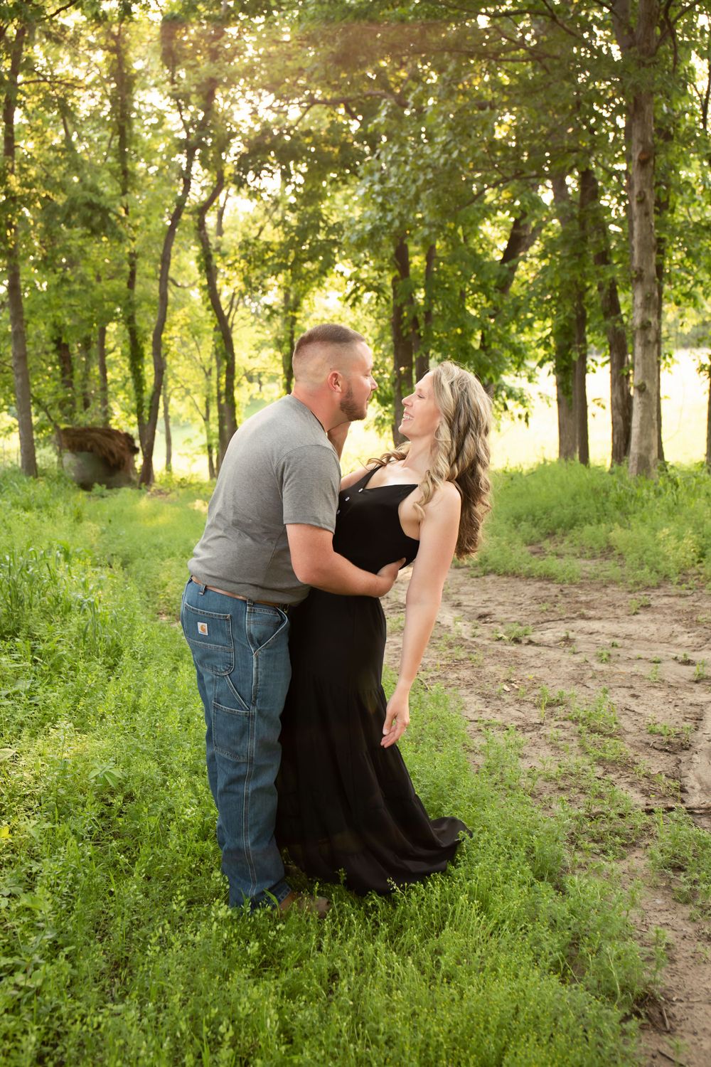Couple shares a romantic moment in a wooded setting with golden sunlight filtering through trees.