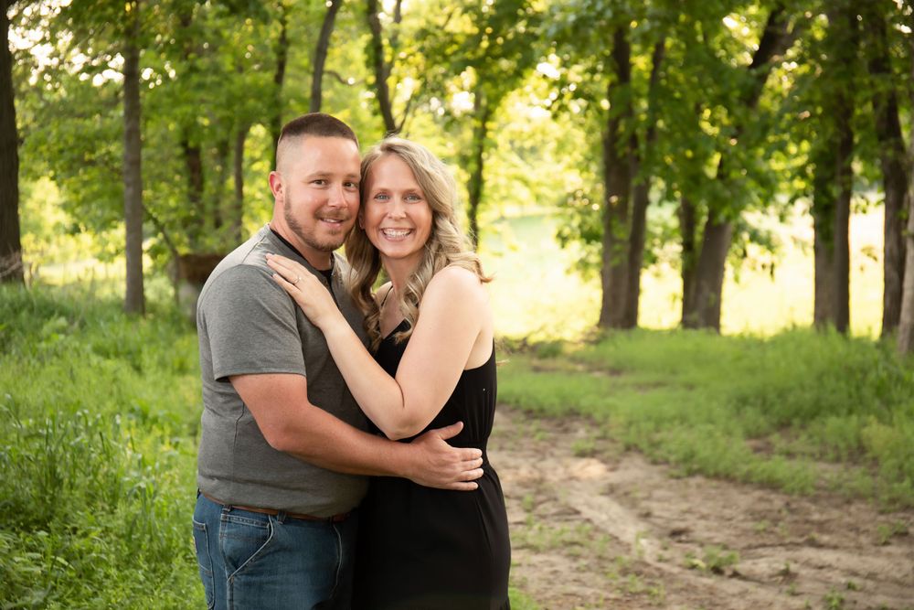 Couple poses together in a wooded setting with natural sunlight creating a warm atmosphere.
