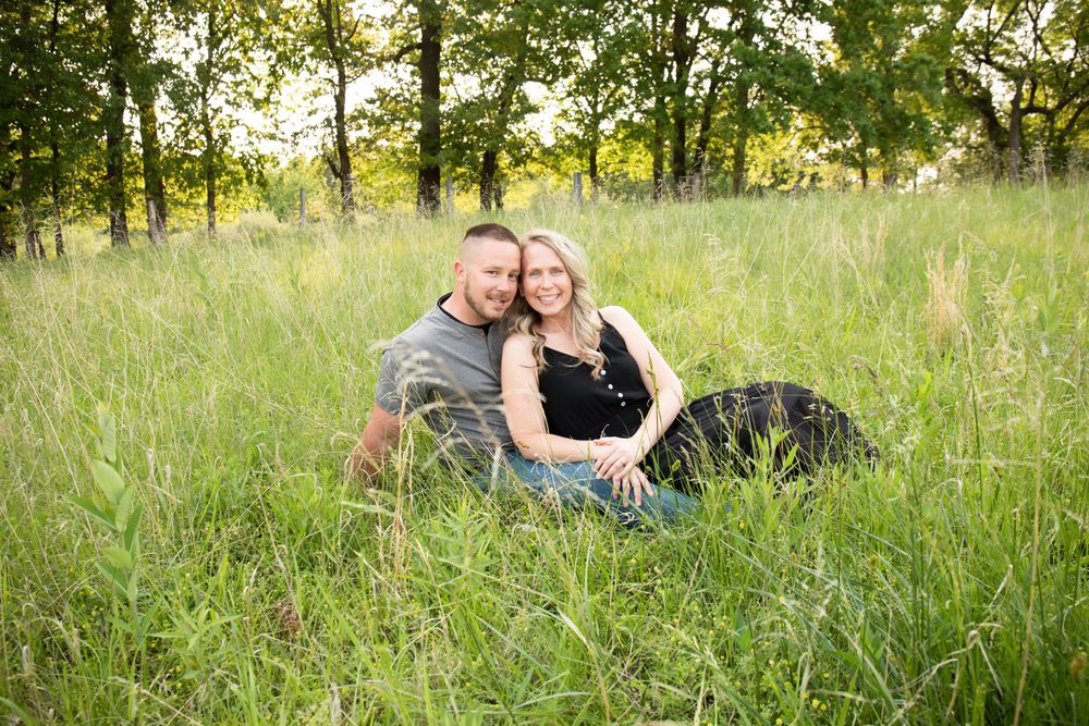 Two people share an intimate moment while sitting in a grassy field during golden hour.