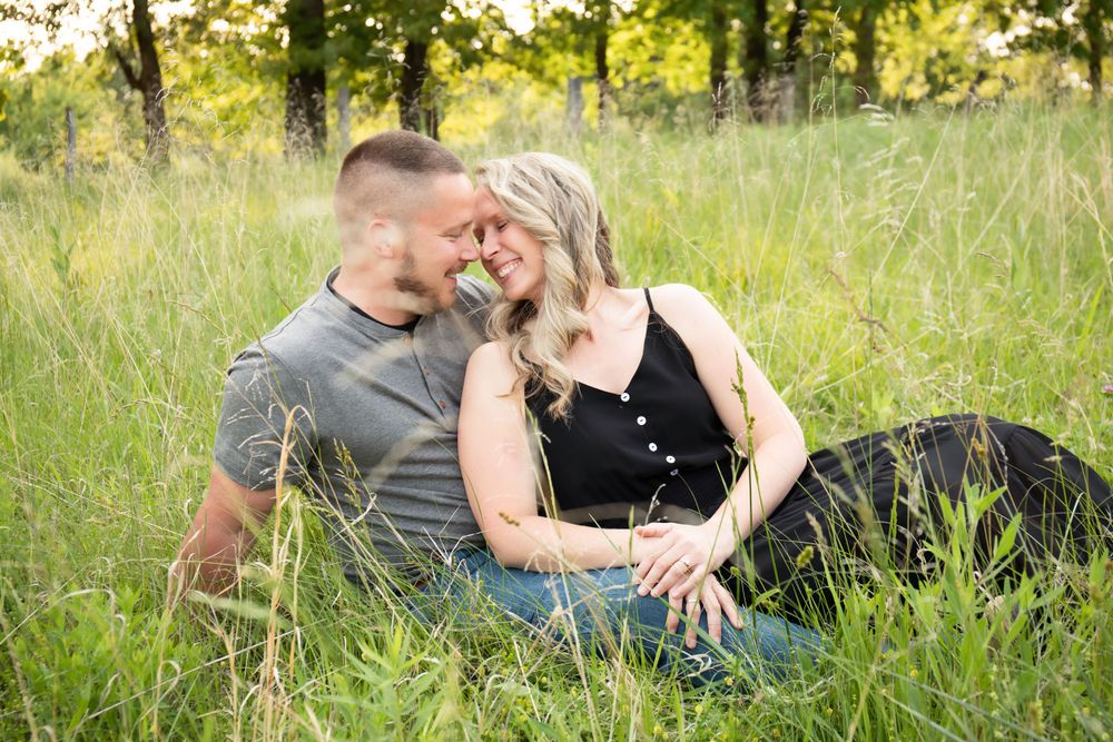 A romantic couple embraces while sitting in a summer meadow with dappled sunlight.