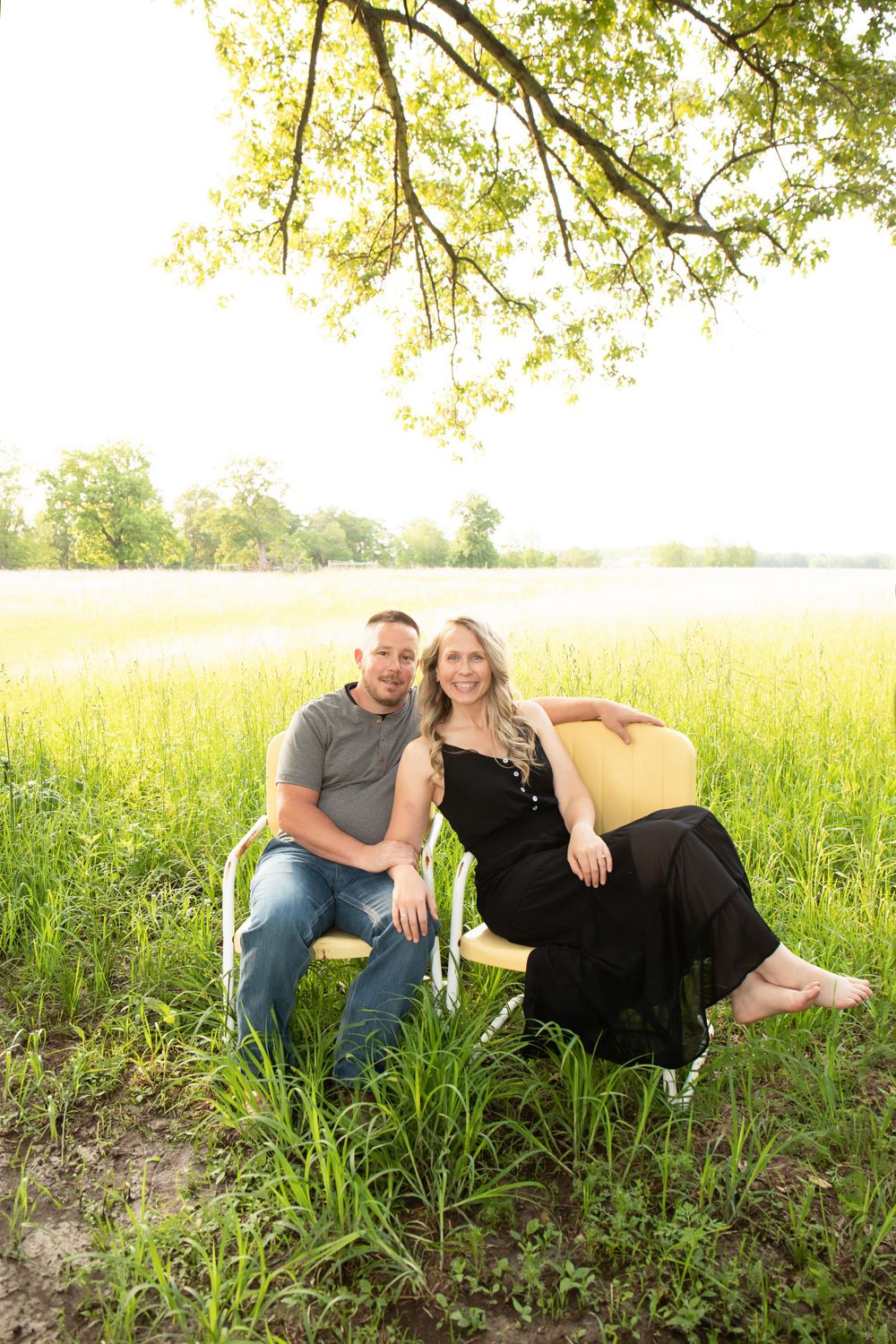 A couple relaxes in a sunny meadow with golden light filtering through tree branches.