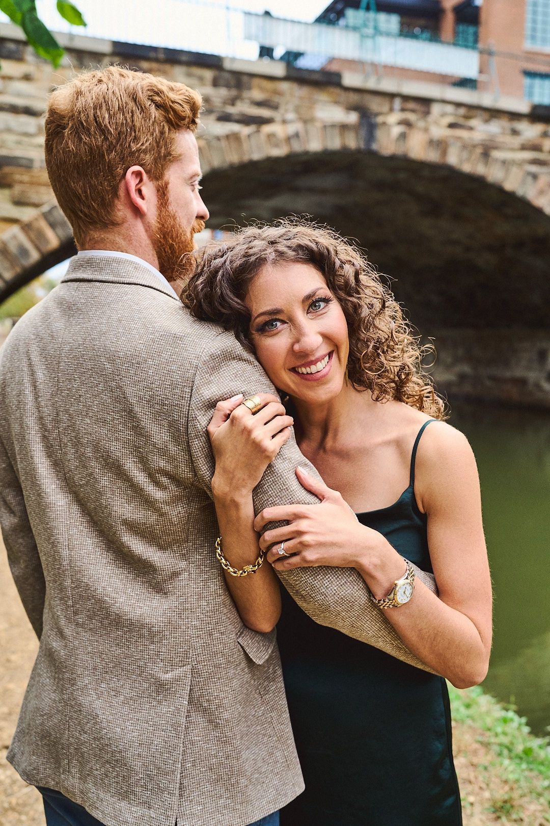 Romantic couple embracing by stone bridge with woman in black dress laughing joyfully.