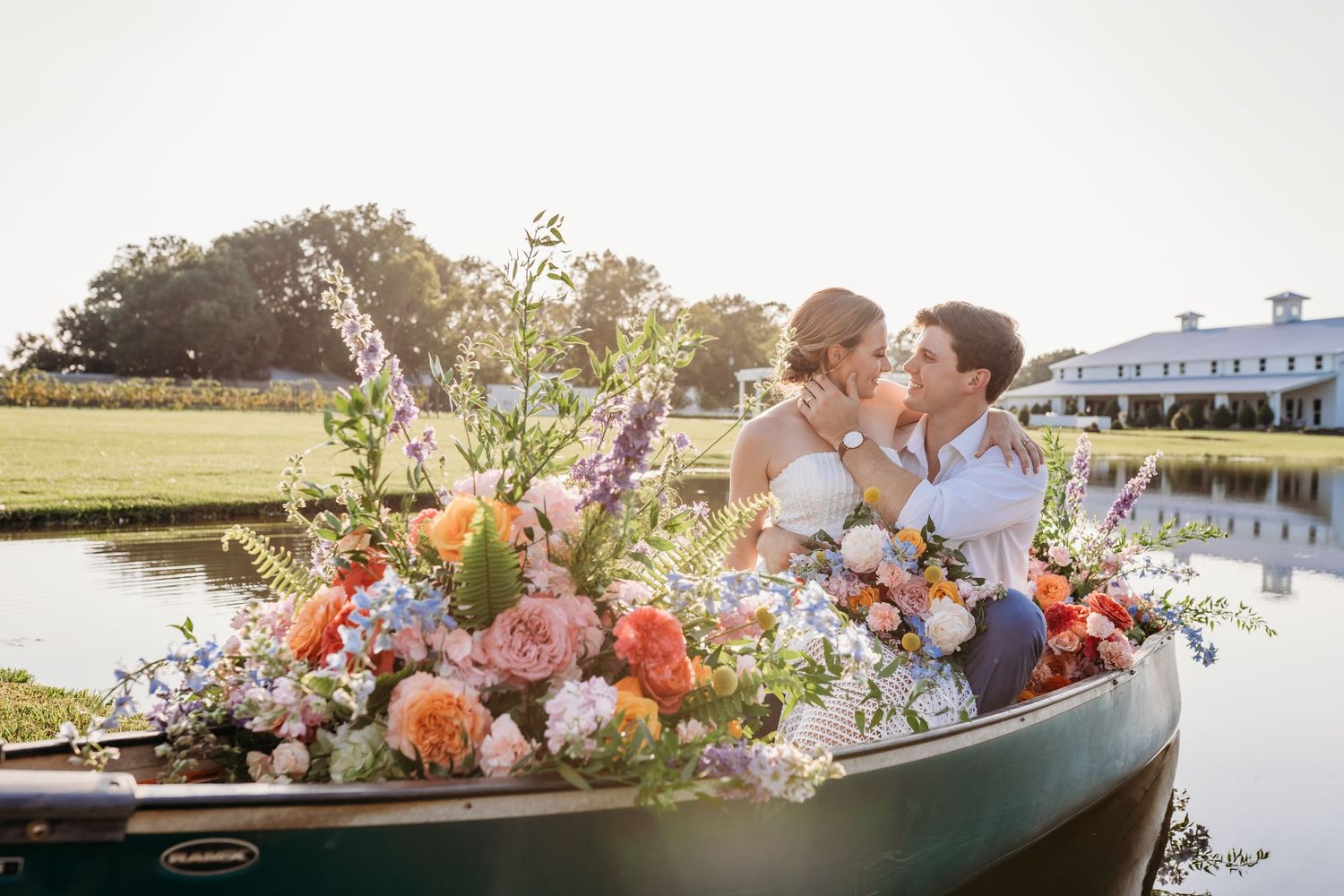 Couple in boat surrounded by vibrant floral arrangement on peaceful water at sunset.