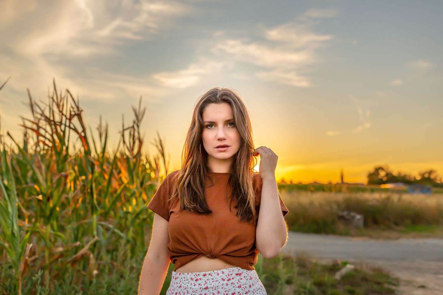 A warm sunset photoshoot in a cornfield with a rustic brown top and patterned skirt.
