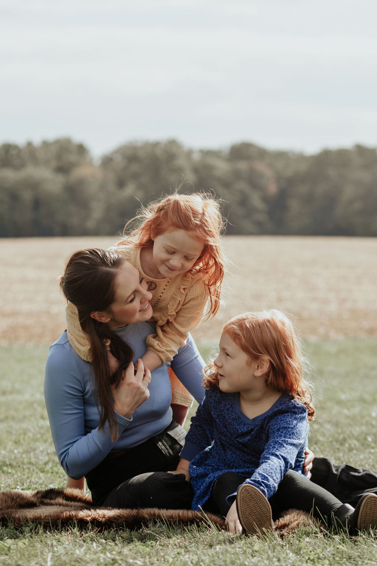 Family enjoying a tender moment together while sitting on a blanket in an autumn field.