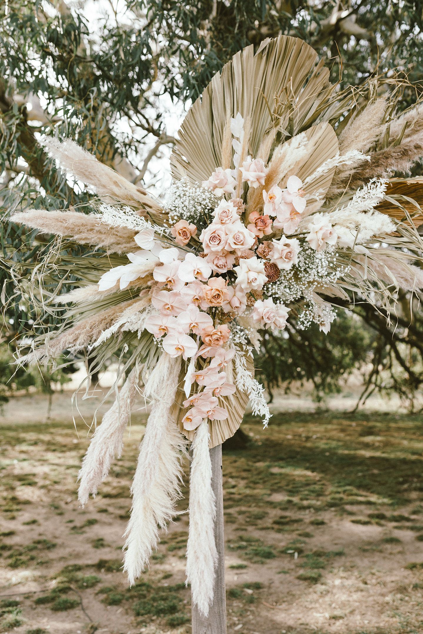 Bohemian wedding arch decoration with dried palm leaves, pampas grass, and blush roses in ethereal arrangement.