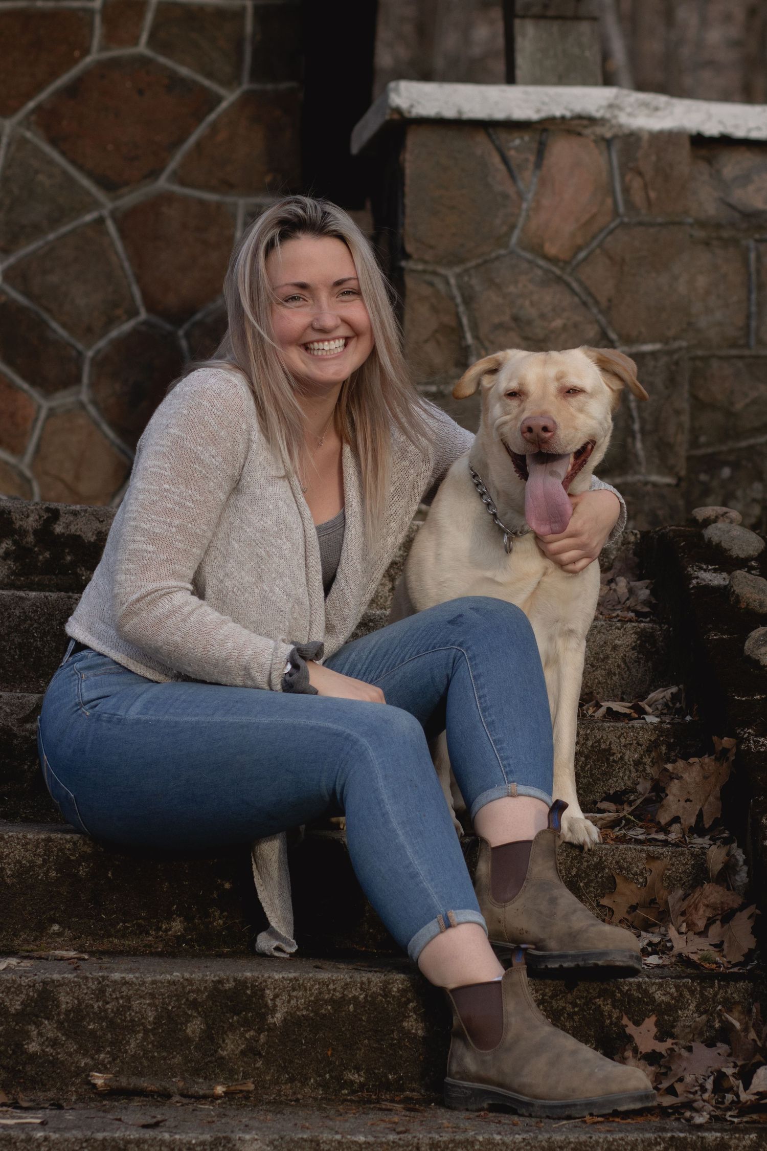 A person and their happy dog sitting together on stone steps against a rustic wall.
