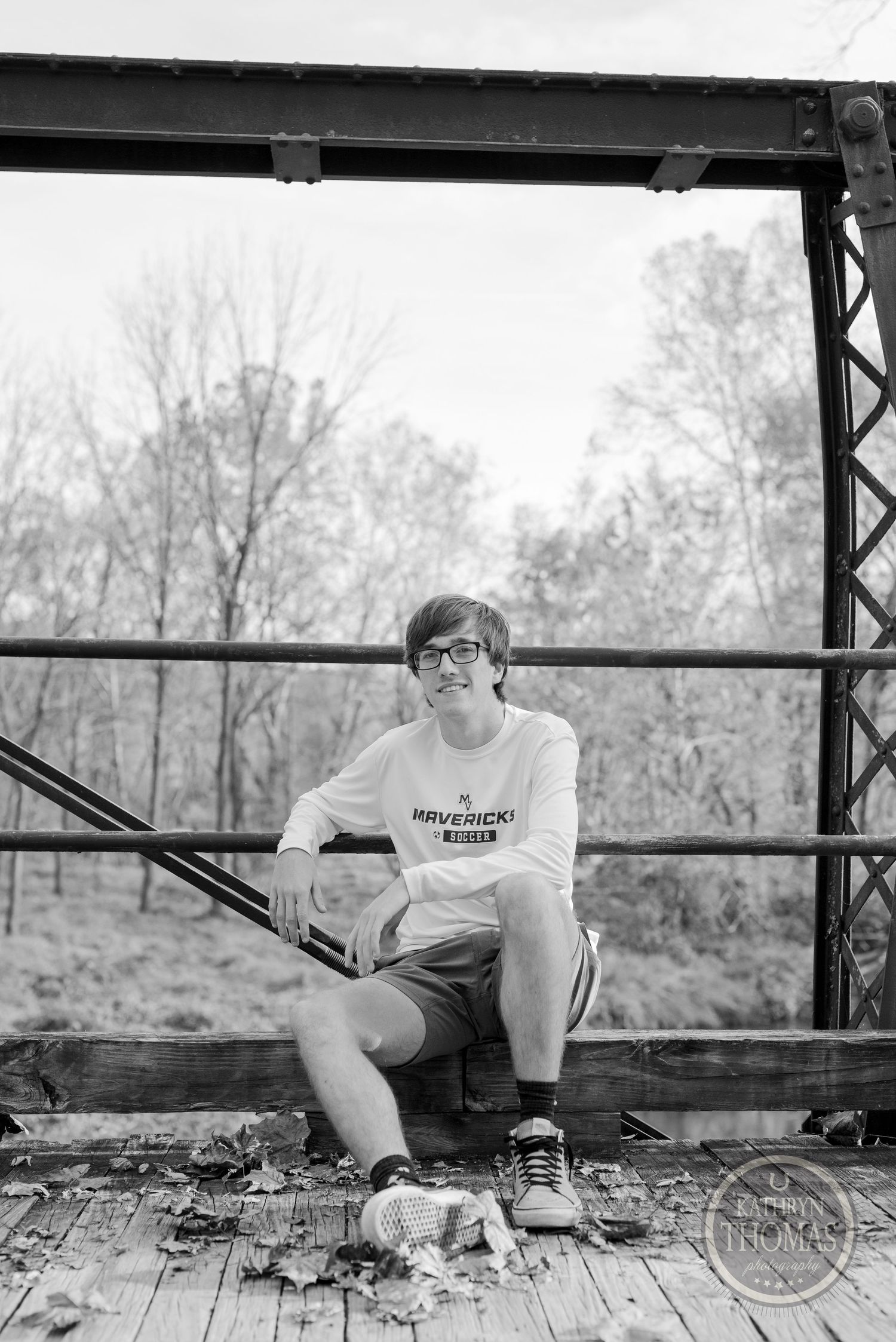 A black and white photo of someone sitting on a wooden bridge with metal support beams.