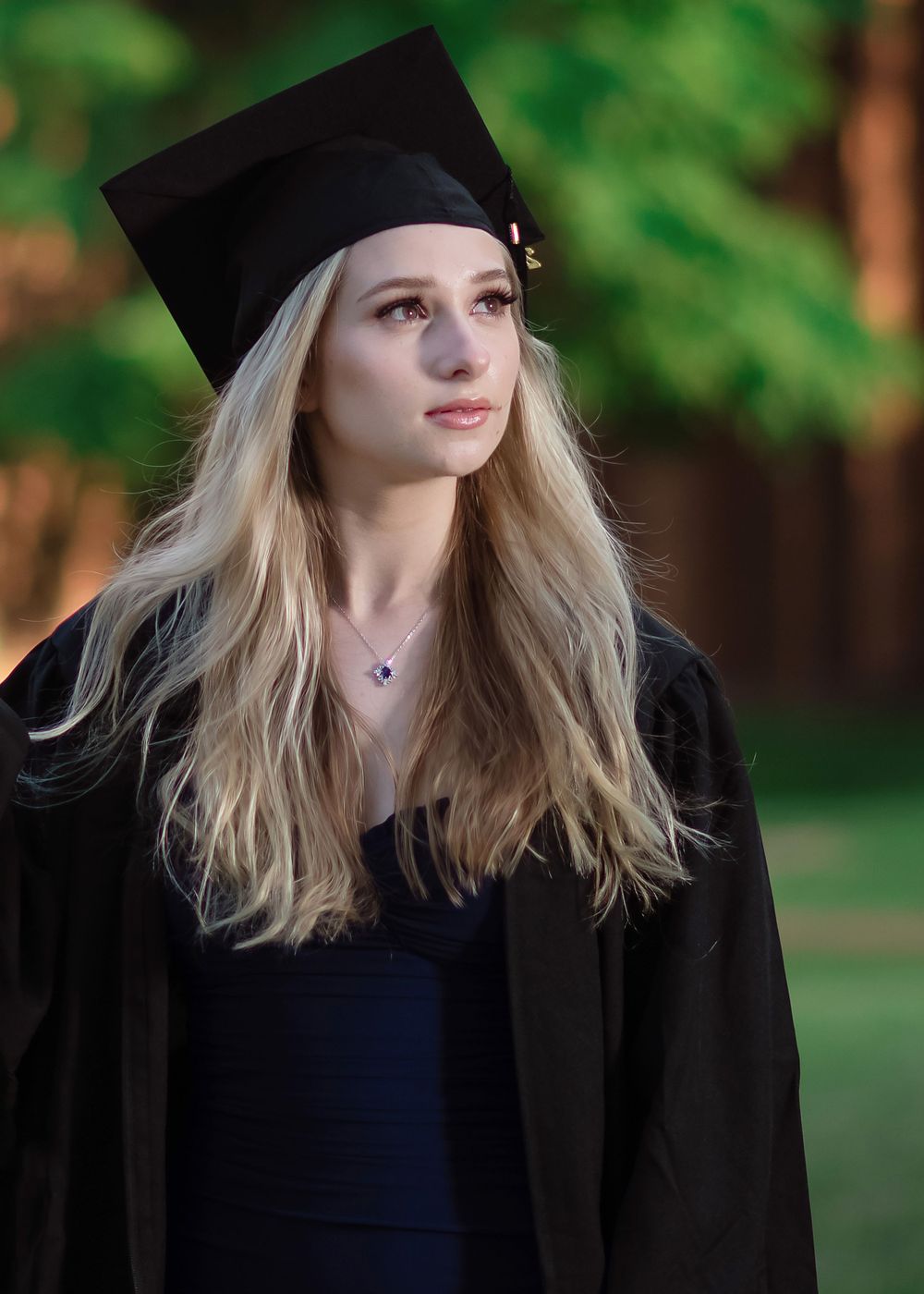 Graduation portrait in cap and gown against green natural background.
