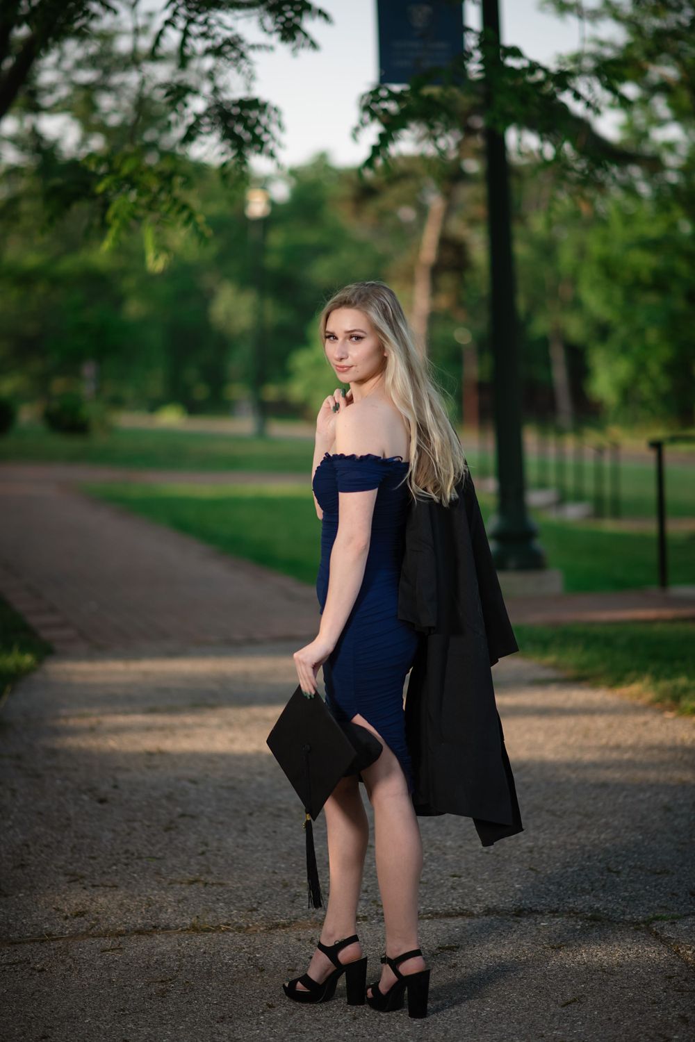 Fashion portrait series on gravel path with person in navy dress and black jacket.
