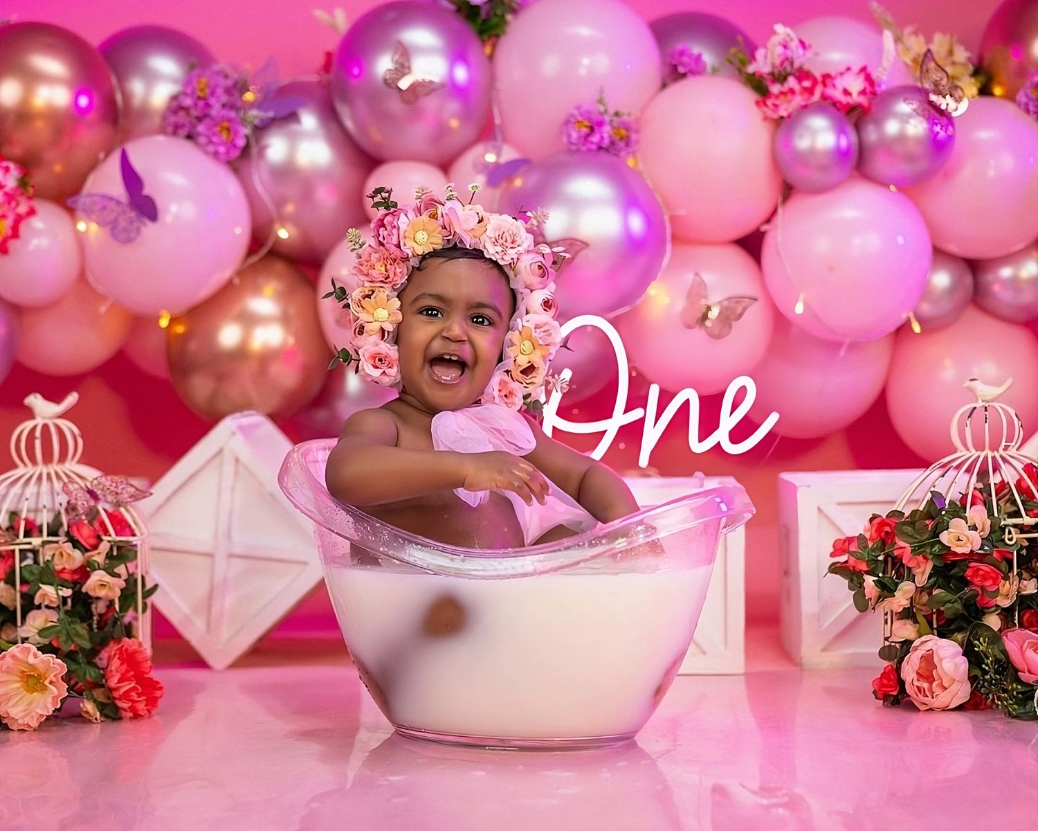 Pink and floral themed first birthday photoshoot with bathtub prop and balloon arch.