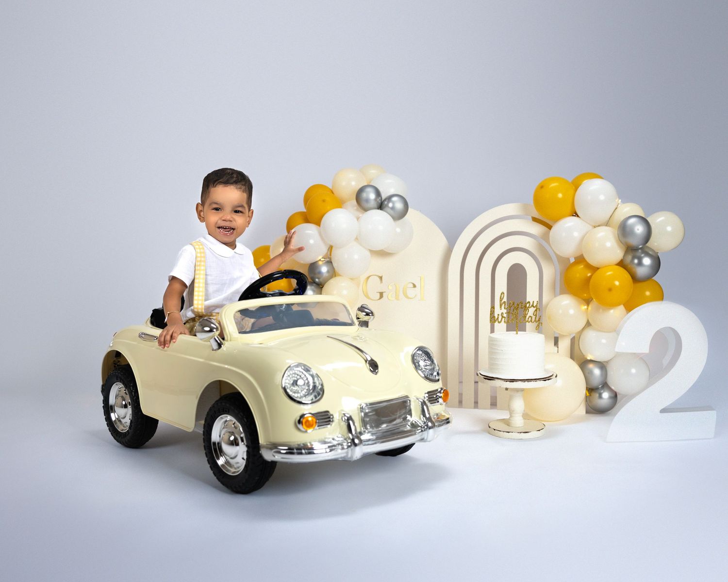 Birthday photoshoot with cream vintage toy car and yellow balloon arch decoration.