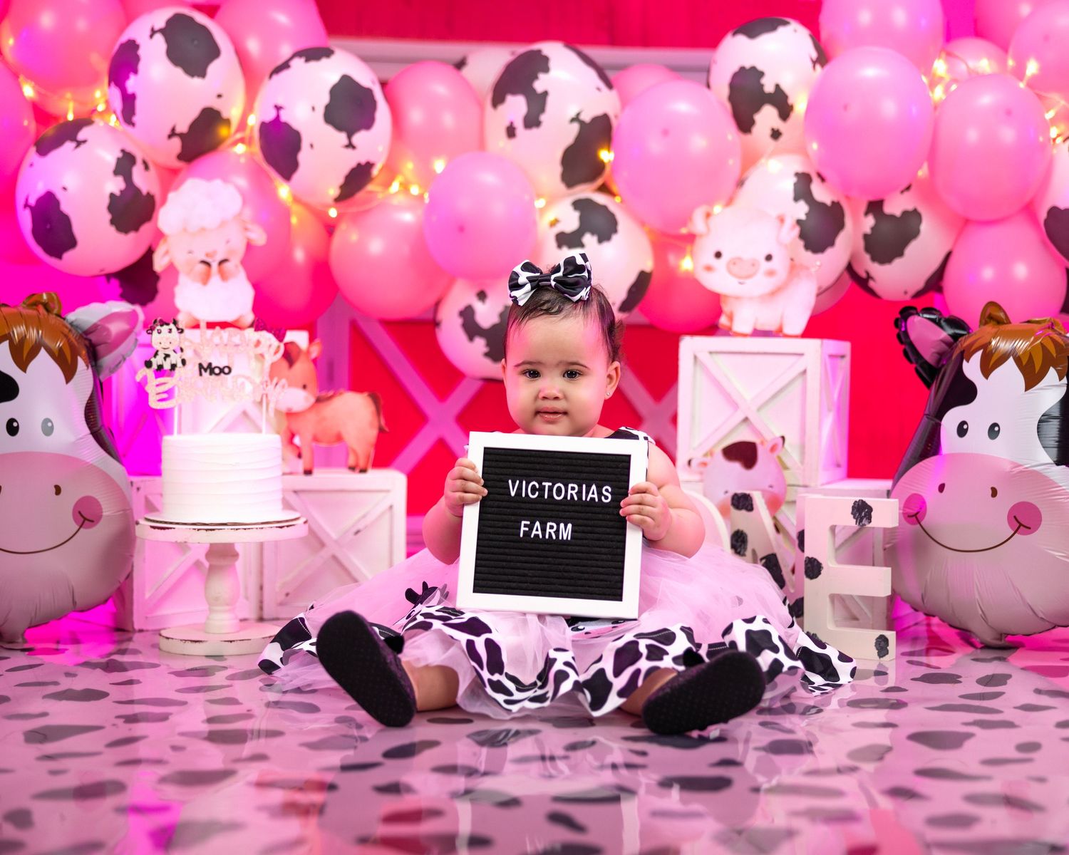 Pink cow-themed birthday setup with matching balloons and cake decorations.