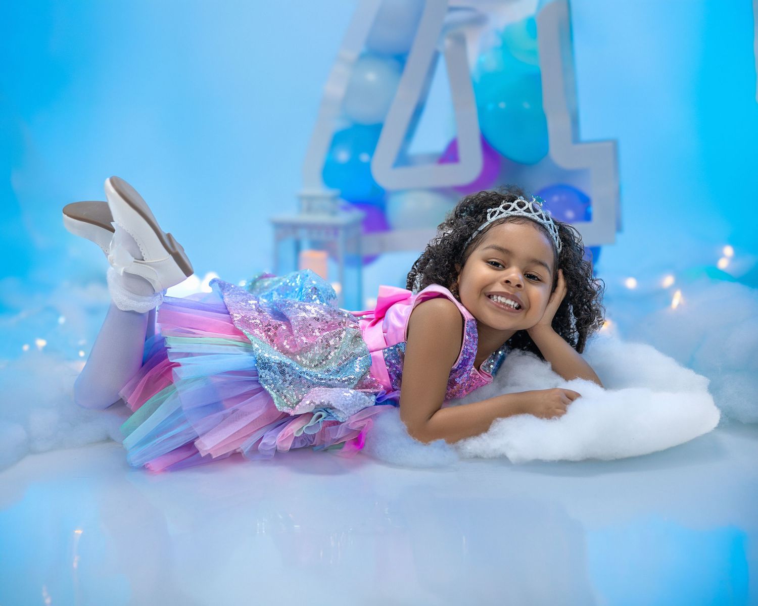 Young child in a sparkly pastel tutu dress laying on fluffy white clouds with number 4 decoration in background.