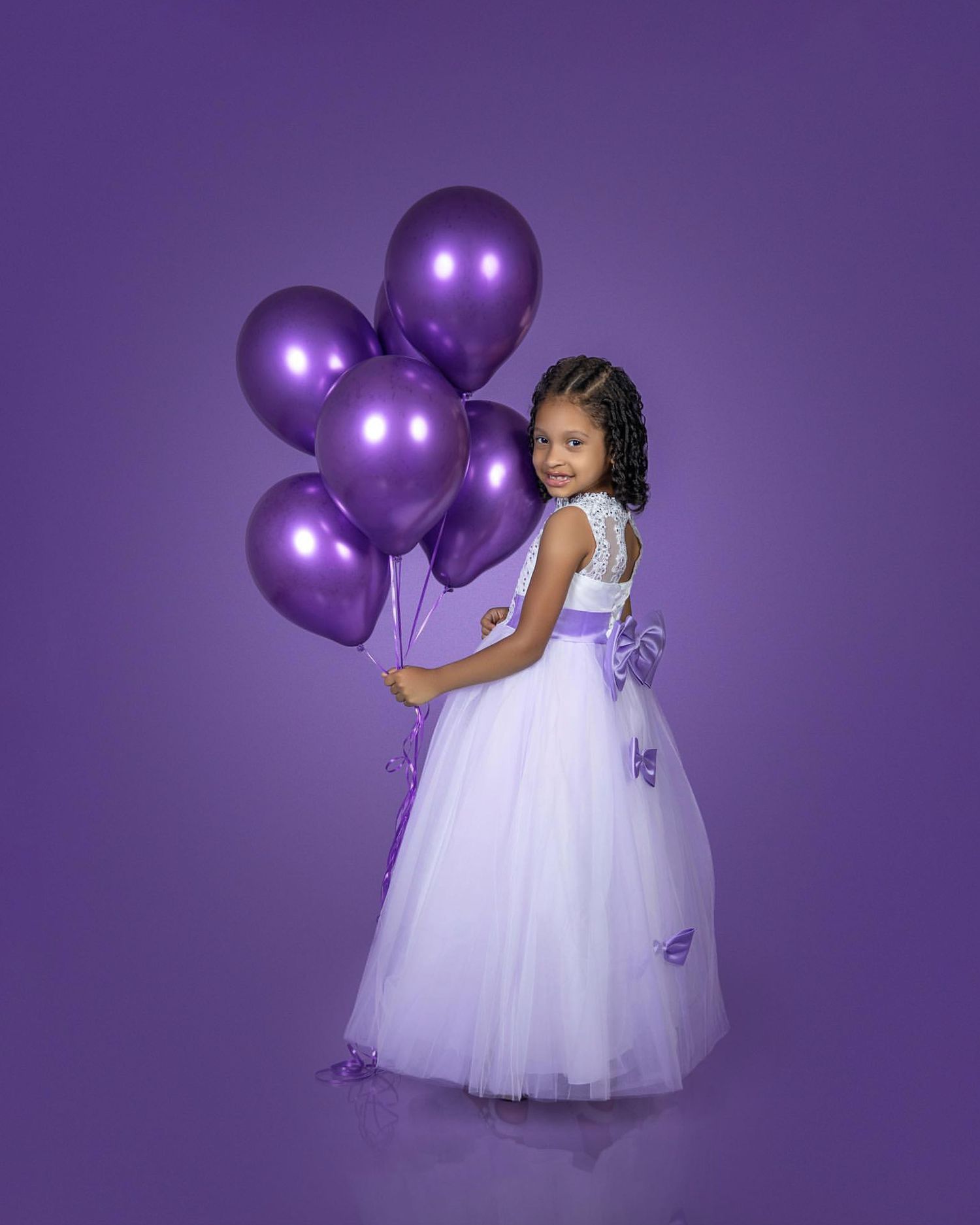 Elegant portrait with purple balloons and white formal dress against purple background.
