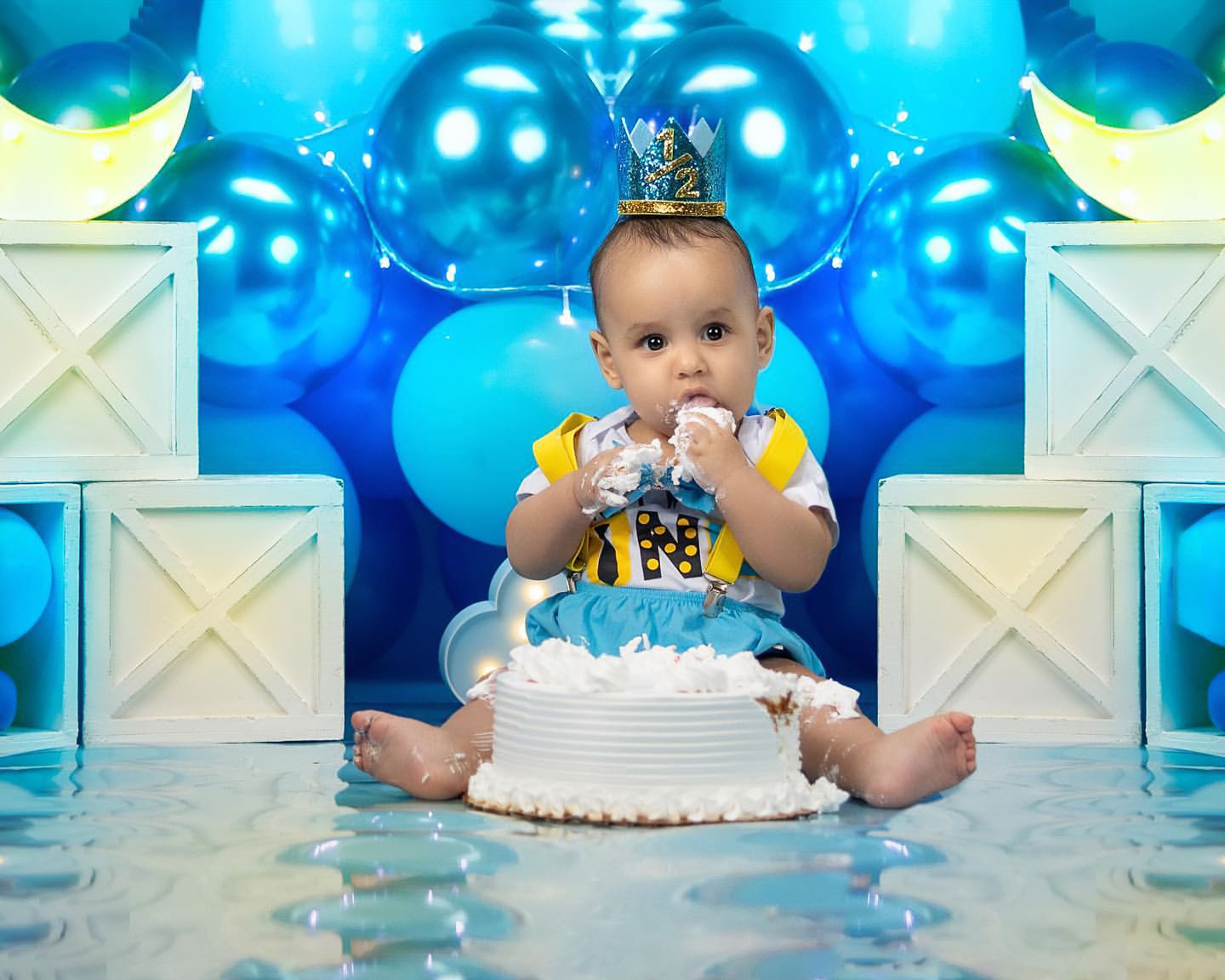 First birthday celebration with white cake and blue balloon backdrop decorations.